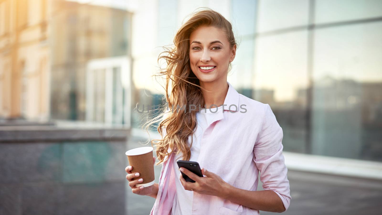 Businesswoman standing summer day near corporate building using smartphone teeth smiling Business person Outdoors Successful european caucasian woman freelancer dressed white shirt pink jacket