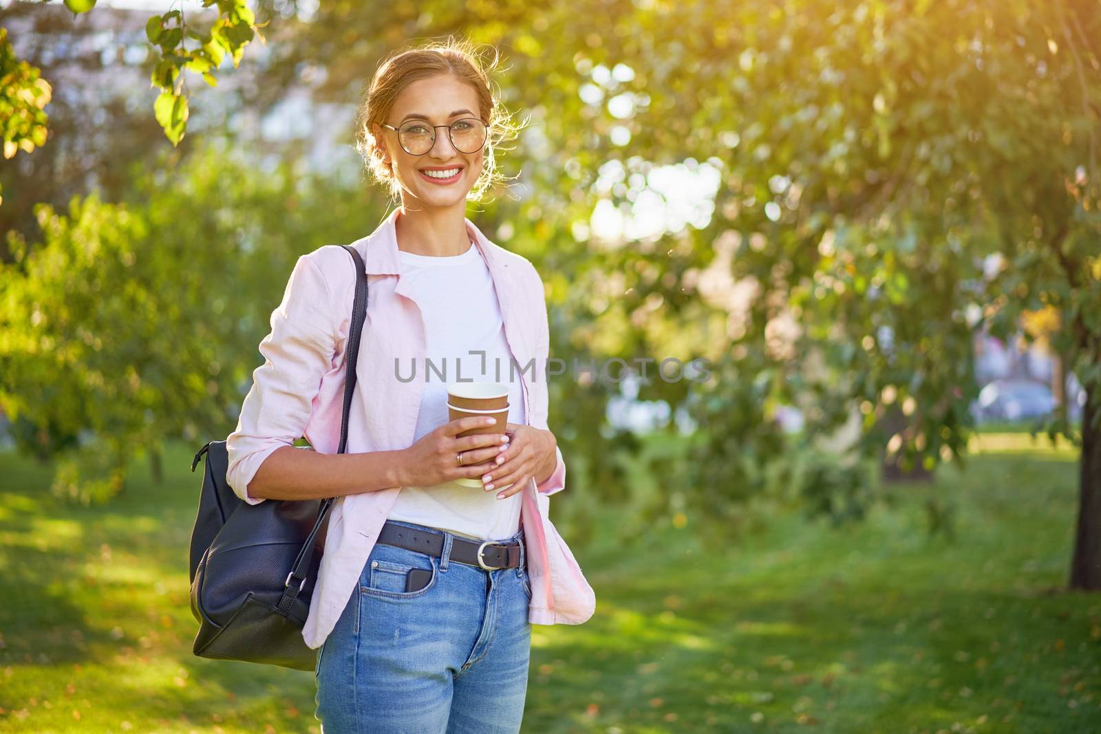 Businesswoman standing summer park Business person Outdoors Successful european caucasian woman freelancer or teacher walking outside with black backpack dressed denim jeans white shirt pink jacket