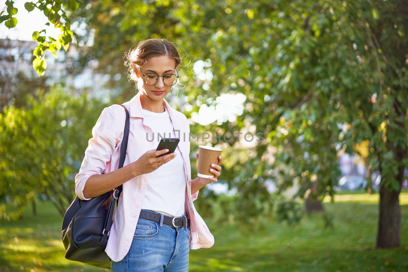 Businesswoman standing summer park Business person using smartphone Outdoors Successful european caucasian woman freelancer or teacher walking outside backpack dressed jeans white shirt pink jacket