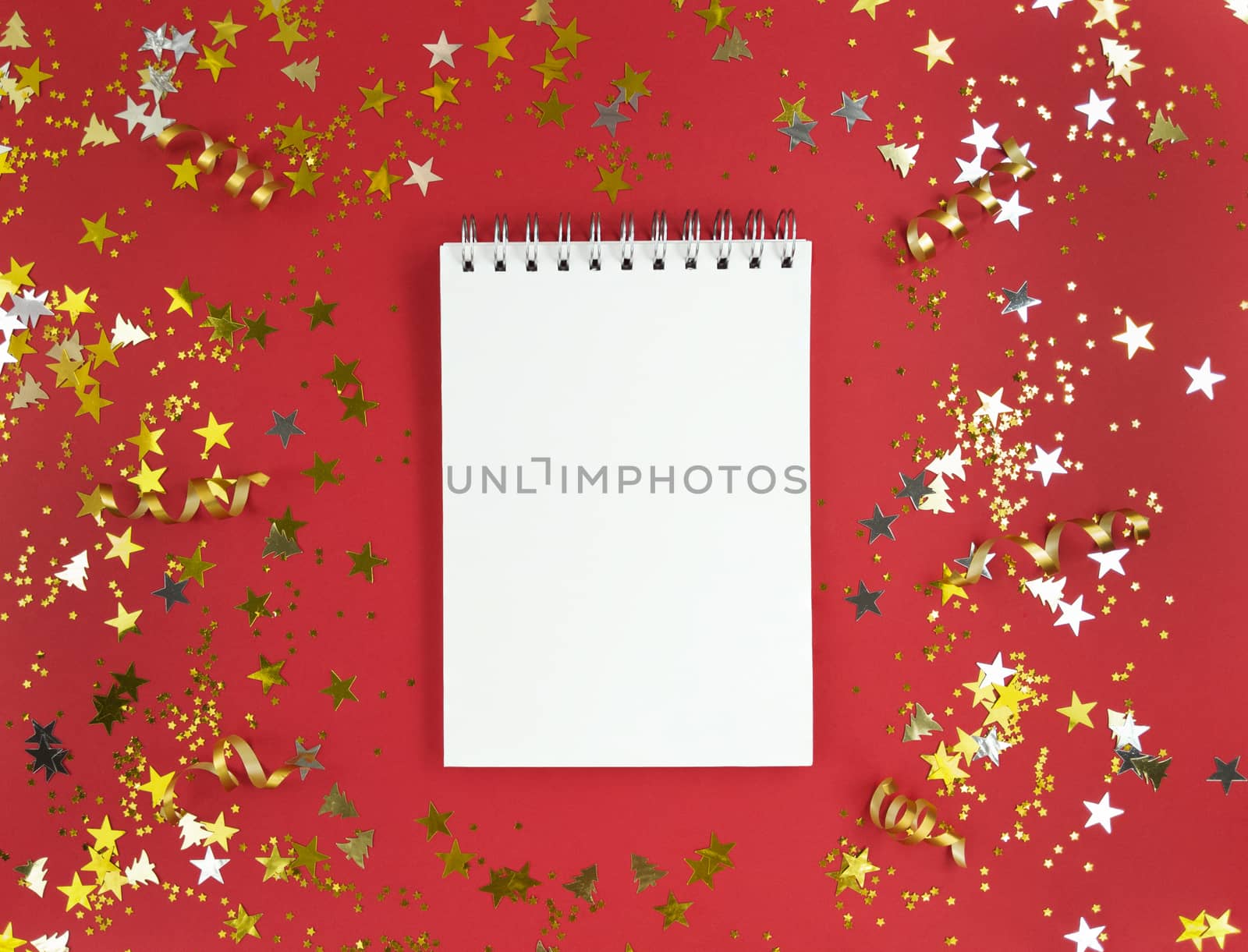 White blank sheet of notebook on red background with scattered confetti. Holiday education concept. Stock photo.