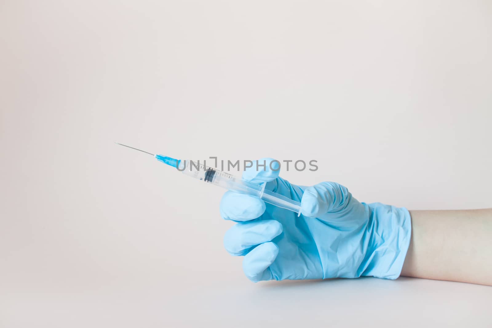 Syringe in hands in protective medical rubber gloves on a light background.