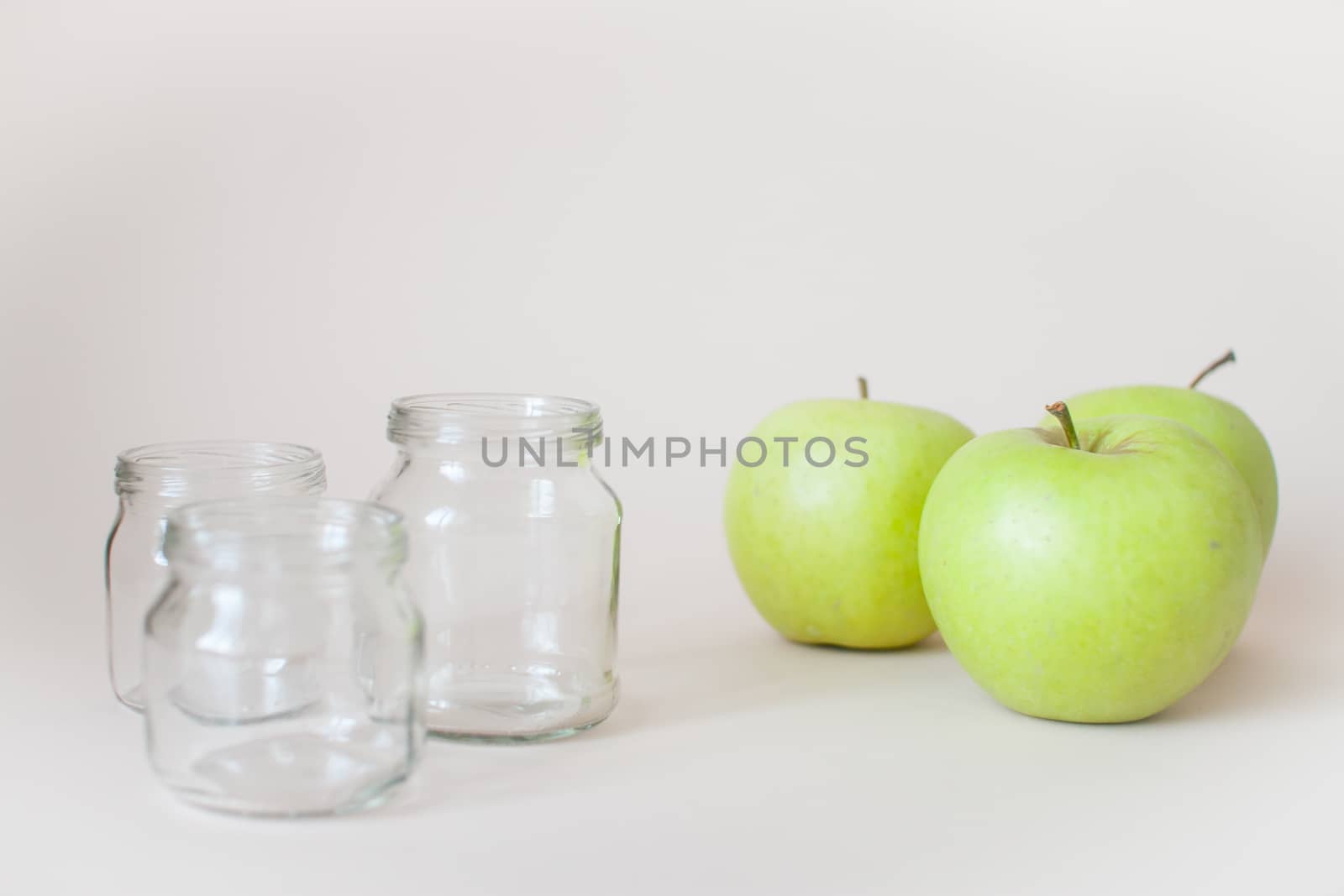 Green ripe apples and empty transparent jars for baby food on a light background