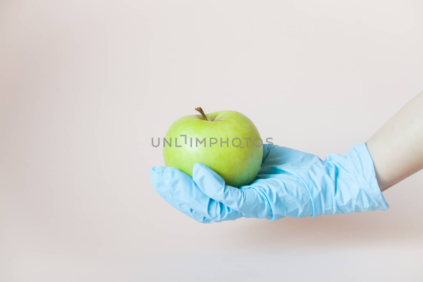 Green apple in hands in protective medical rubber gloves on a light background.