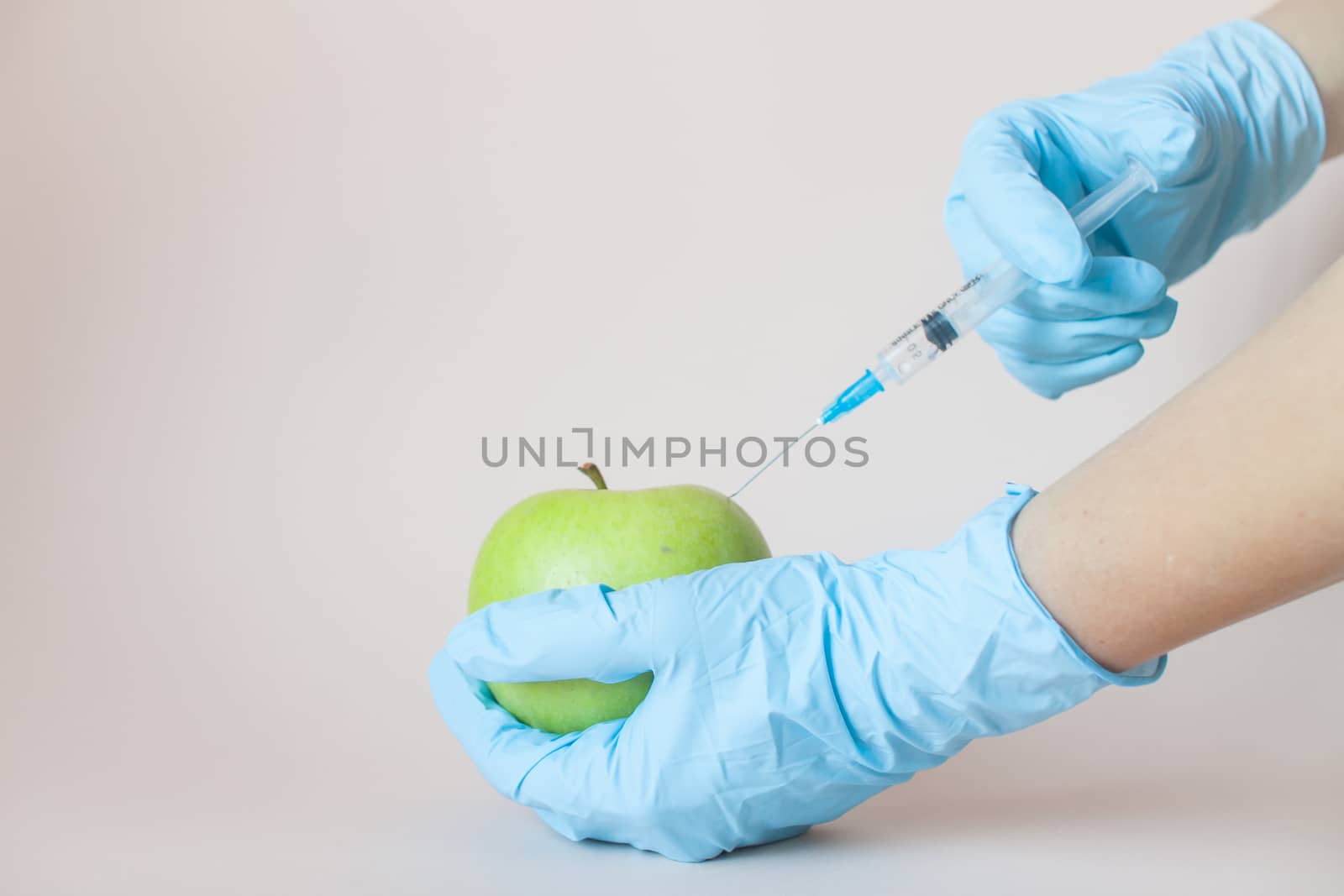 Green apple in hands with a syringe in protective medical rubber gloves on a light background.