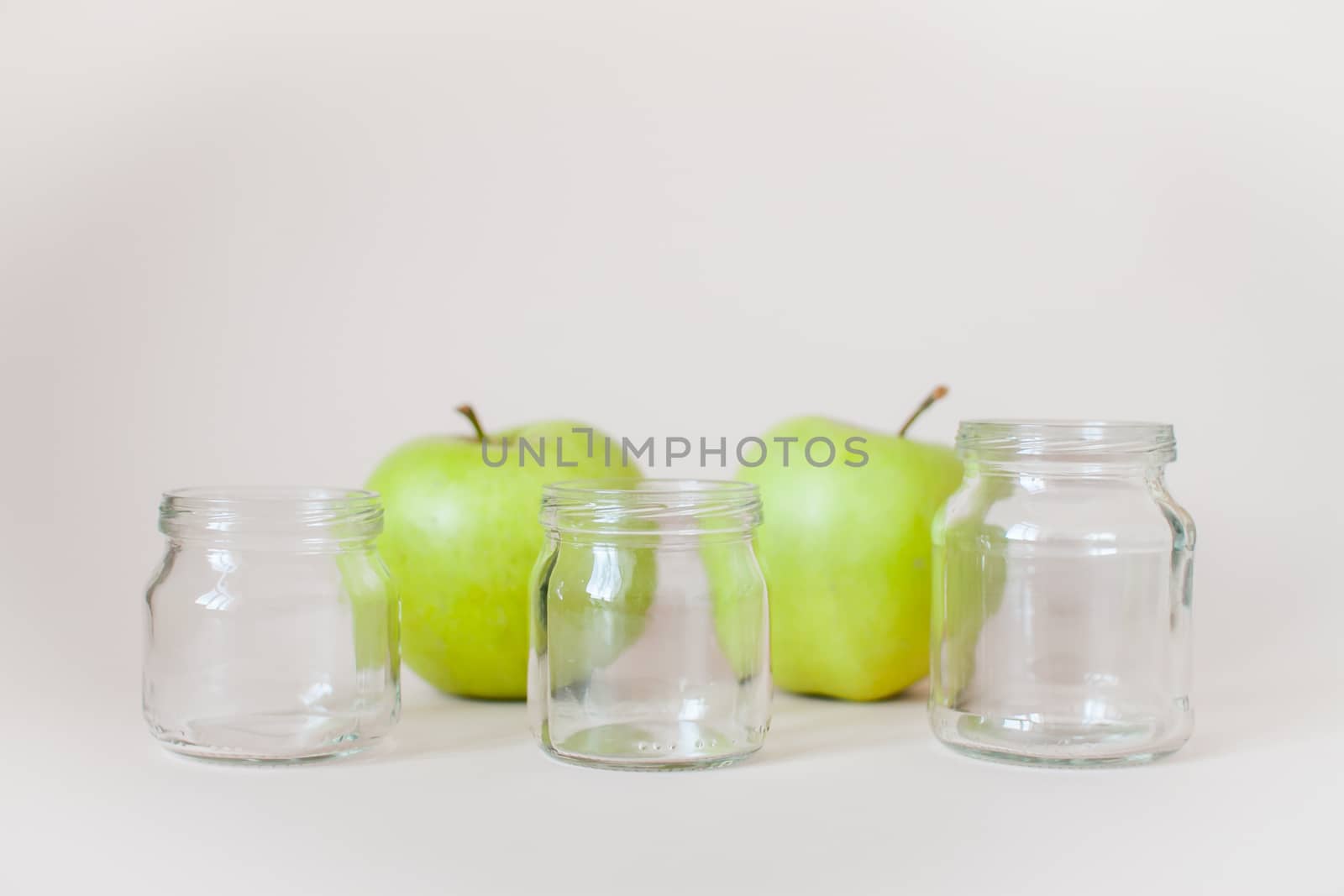 Green ripe apples and empty transparent jars for baby food on a light background