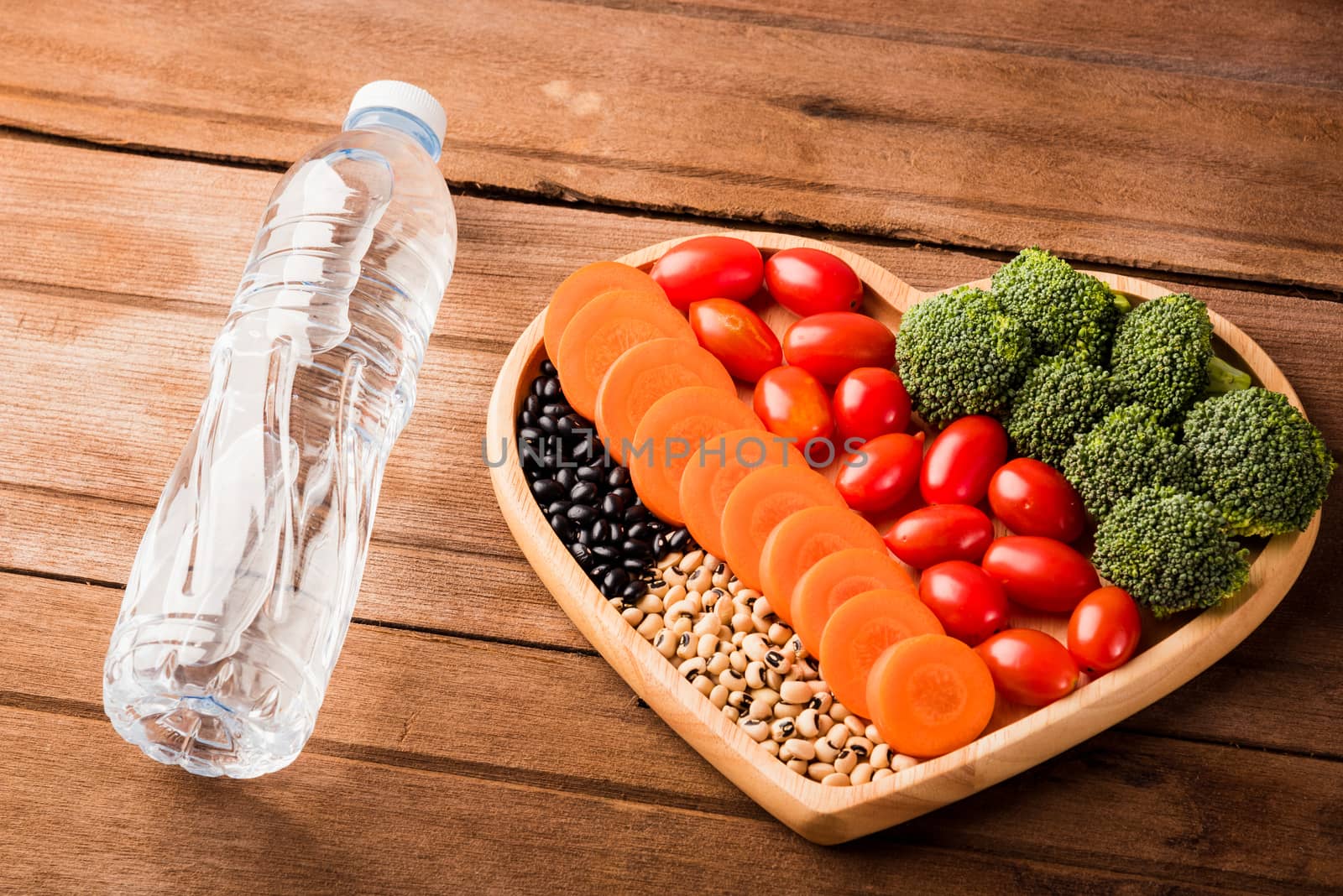 Top view of fresh organic fruits and vegetables in heart plate wood (carrot, Broccoli, tomato) and plastic water bottles on wooden table, Healthy lifestyle diet food concept