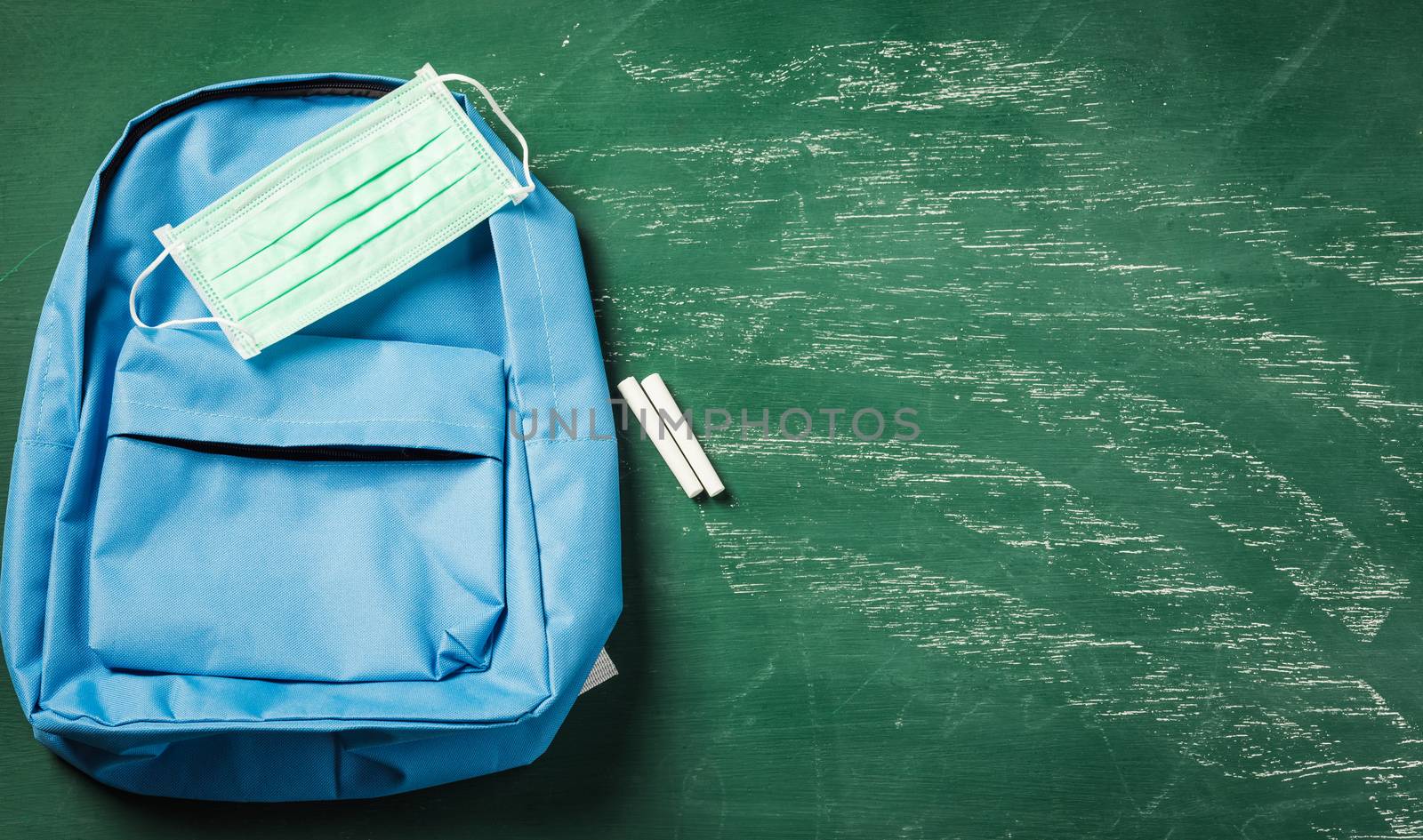 Top view of blue school bag backpack at a green chalkboard with face mask protection and have copy space for your text, Back to school education during epidemic coronavirus concept