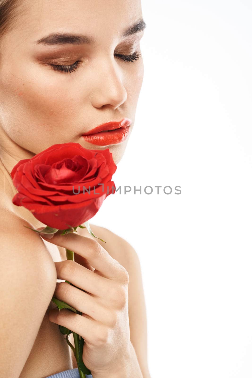 Beautiful woman with red rose near face makeup naked shoulders portrait. High quality photo