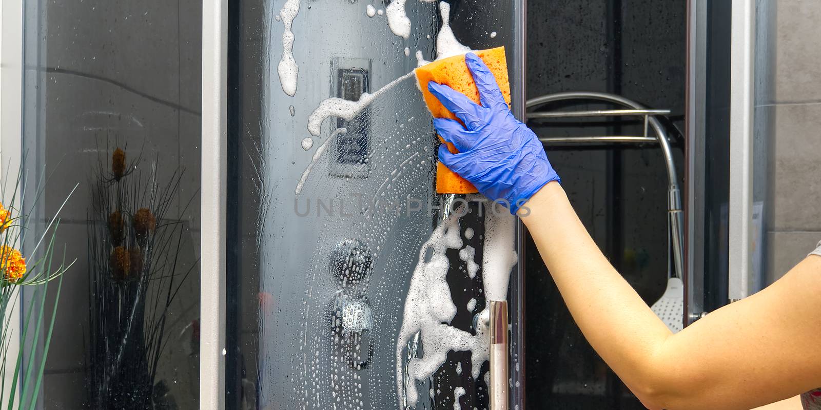 Cleaning of shower steam cabins from Calcium deposits. Cleaning in the bathroom. woman hand in blue gloves with rag and detergent, washing and polishing shower booth from Calcium stone. Maid or housewife cares about house. Commercial cleaning service company concept.