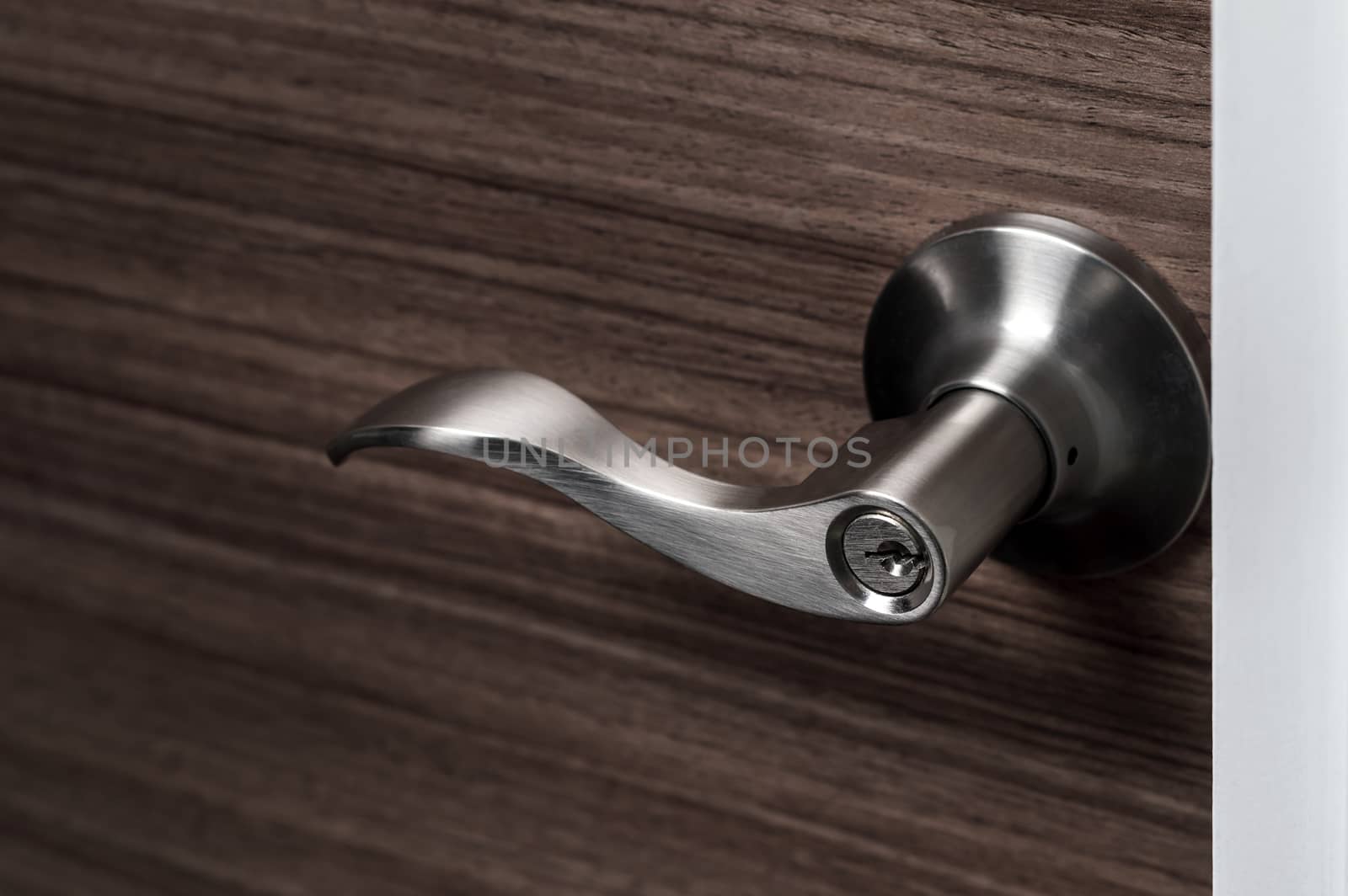 stainless steel door knob or handle with keyhole on wooden door, wave style lever handle front door knob with lock, modern interior design concept, shallow depth of field