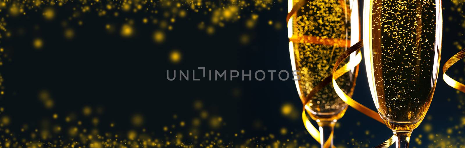 Champagne glasses with golden ribbon on black background with copy space - new year holiday celebration