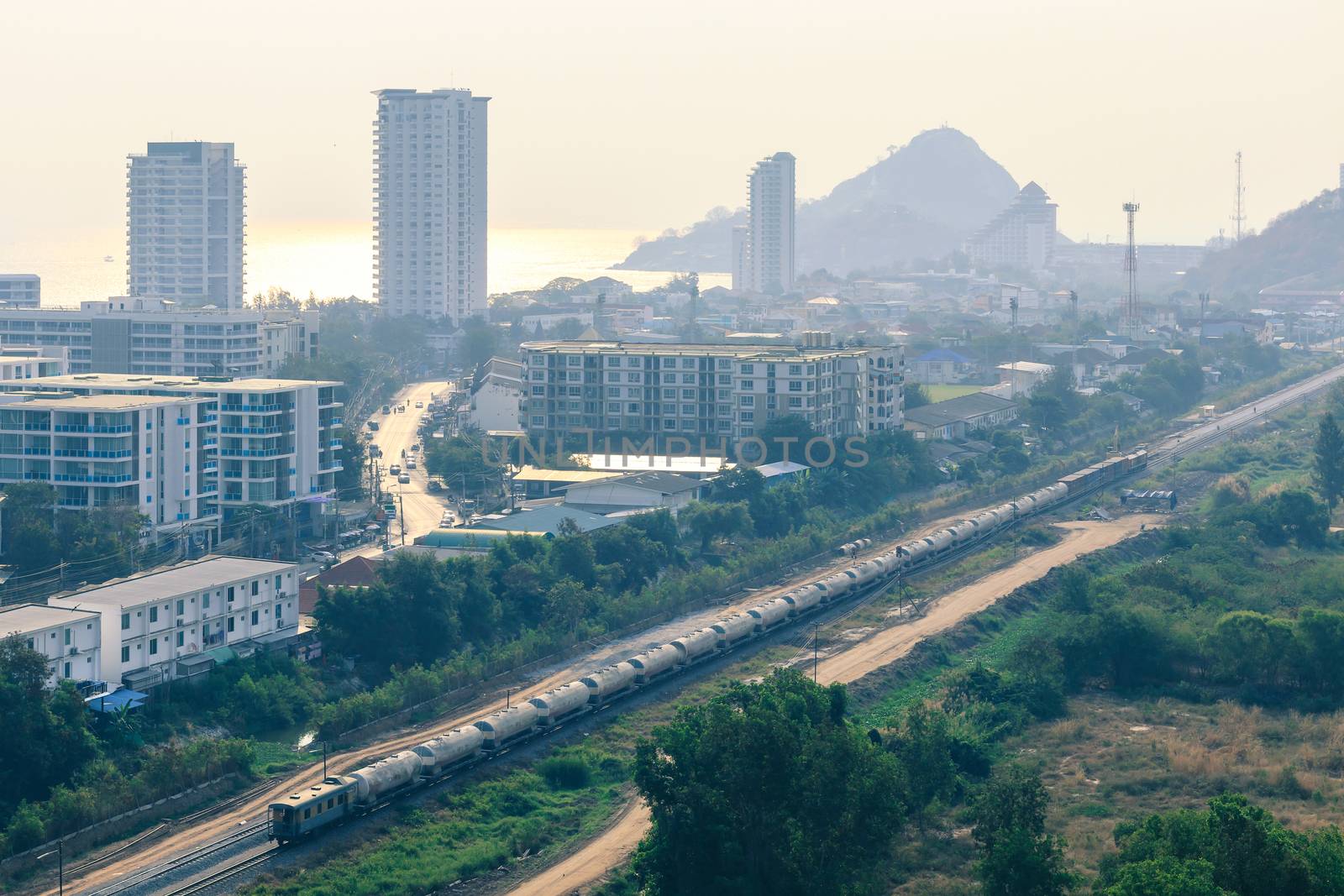 aerial view of train running through small city by the sea in morning sunlight with reflection on water, city in poor weather morning, haze of pollution covering city