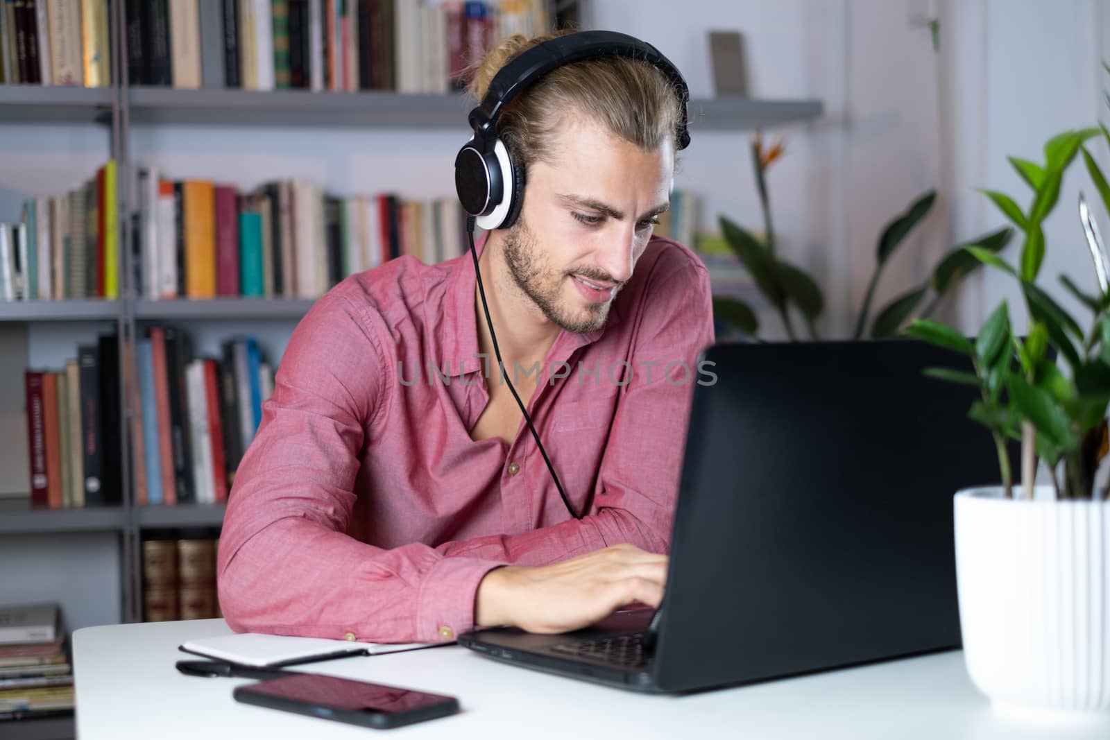 Handsome young caucasian man using computer working at home and talking with headphones feeling happy with smile showing teeth