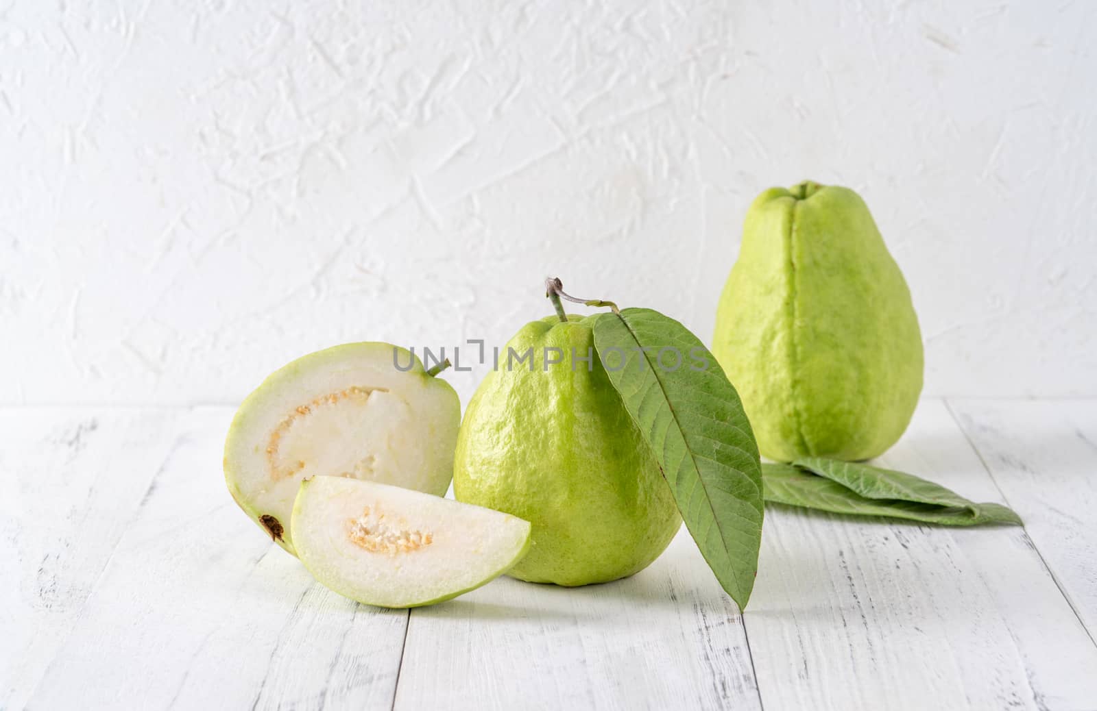 Delicious beautiful guava set with fresh leaves isolated on bright white wooden table background, close up.