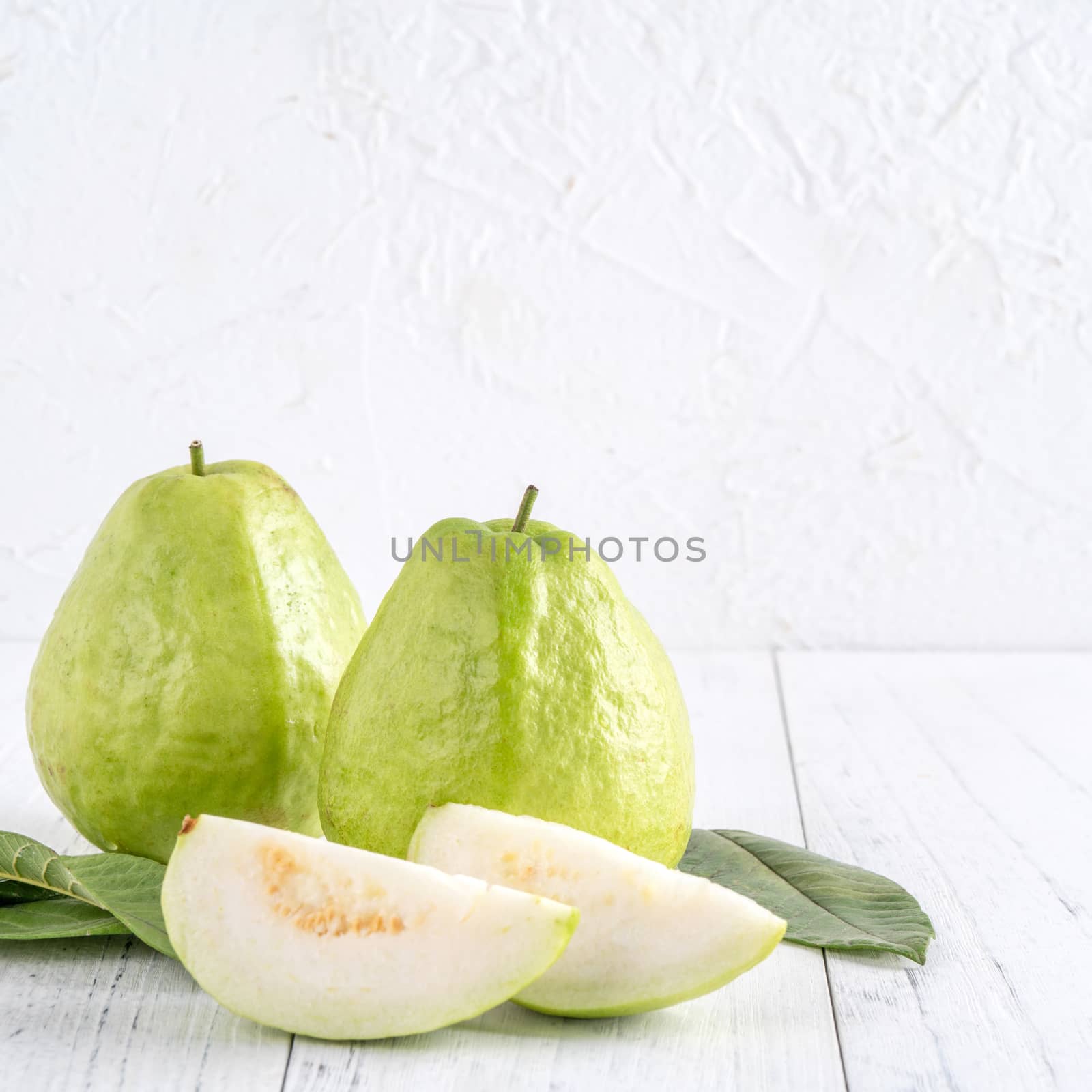 Delicious beautiful guava set with fresh leaves isolated on bright white wooden table background, close up.