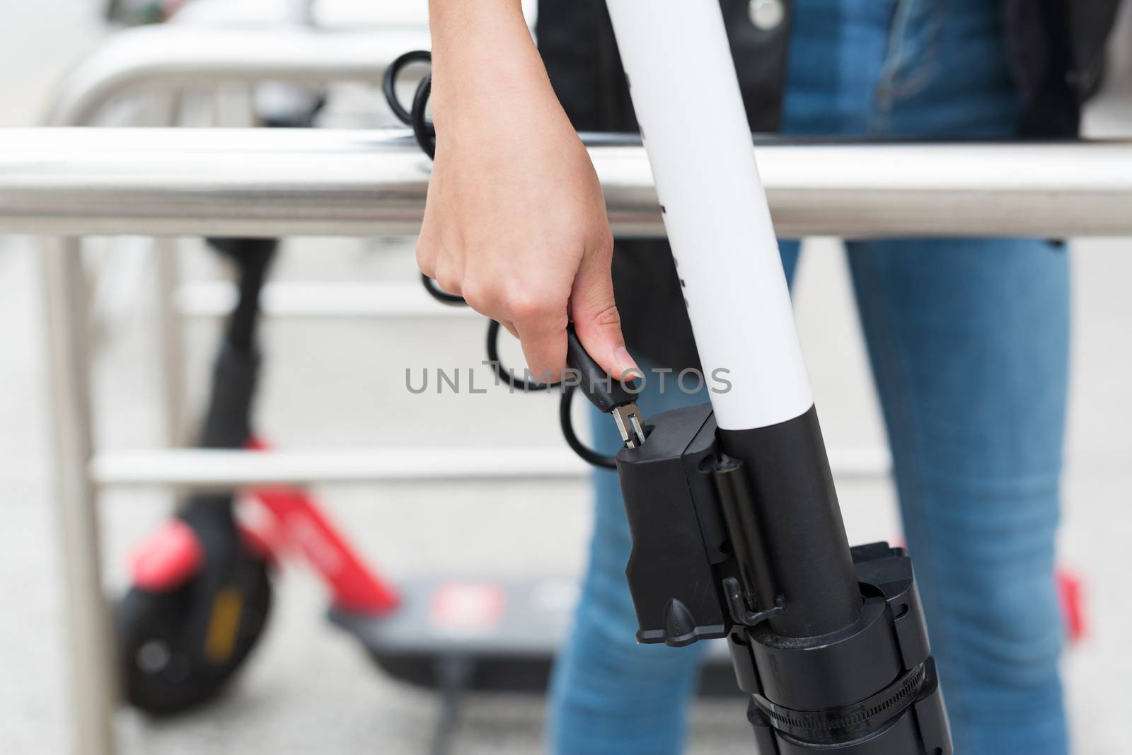 User safely parking electric scooter and locking it to a fence. Eco friendly green modern urban mobility concept of sharing transportation with electric scooters for rent in Ljubljana, Slovenia.