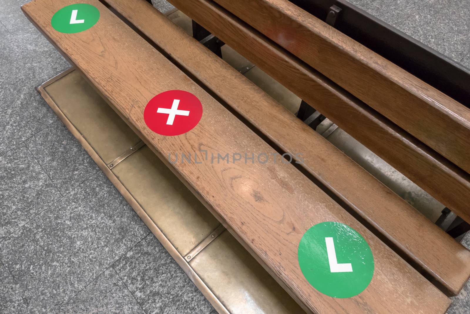 The green dot stickers are being placed on wooden park chair to show people where they can sit while maintaining social distancing. The red color to show people where don't sit. Safety for pandemic covid.