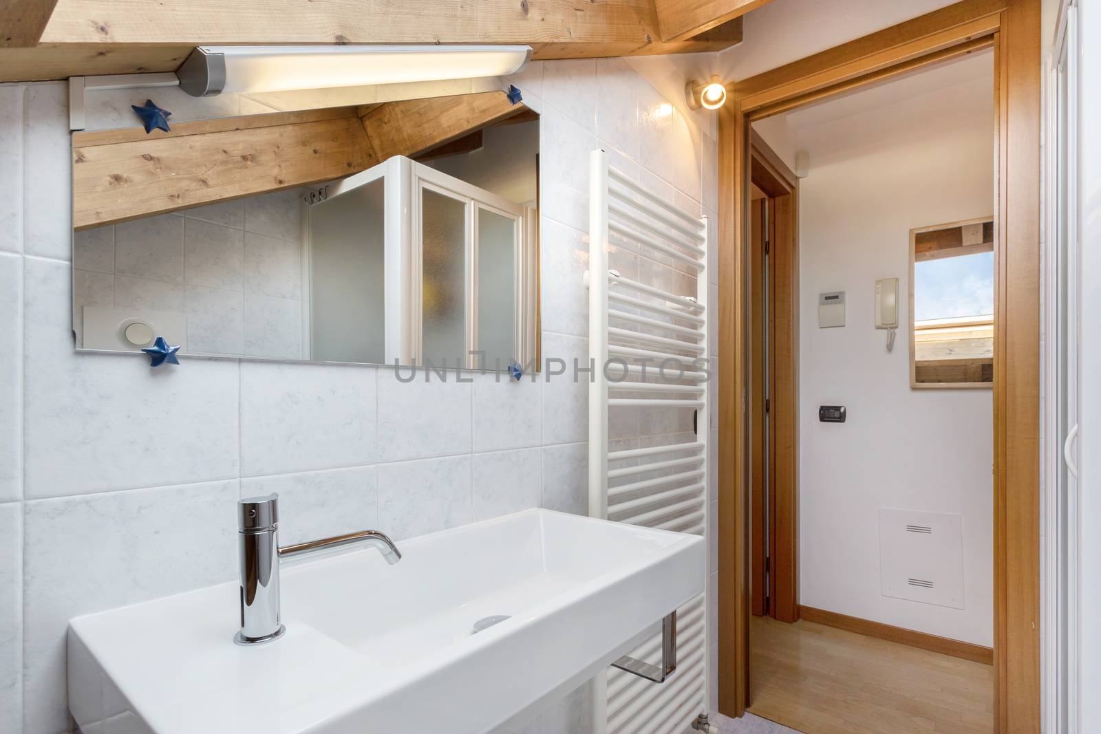 Practical and cozy bathroom with towel radiator, toilet, cabinet and sink. Roof with exposed wooden beams. Classical italian design and style.
