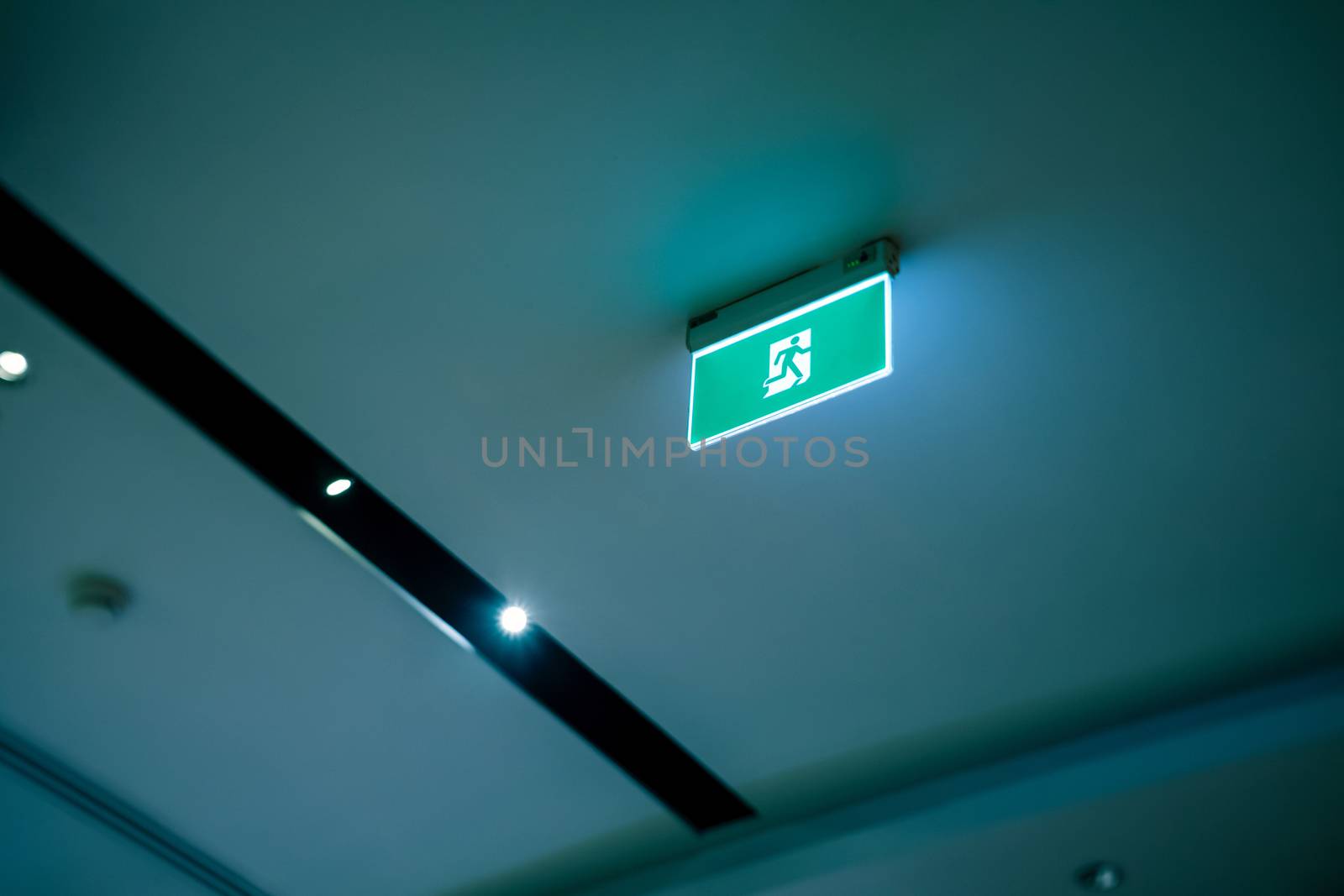 green emergency exit or fire exit hanging sign showing the way to escape from building of hospital or hotel at night time, shallow depth of field