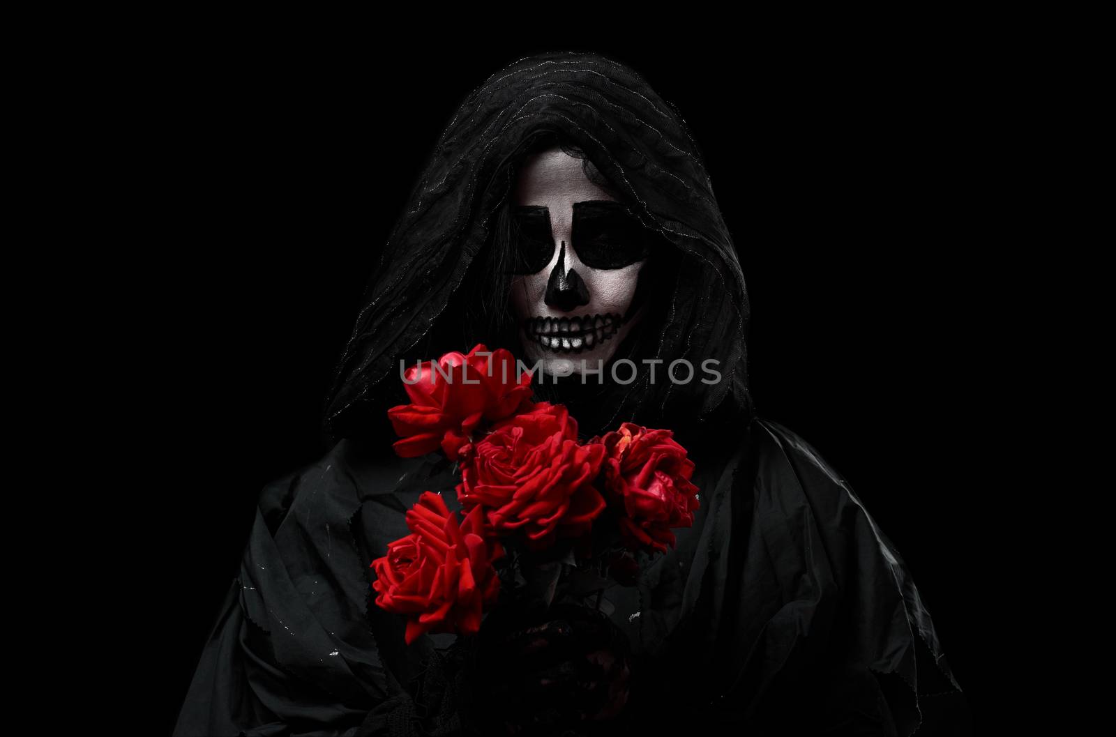 woman in a black hood with a skeleton make-up holds a bouquet of red roses in front of her, an invented image for the Halloween holiday