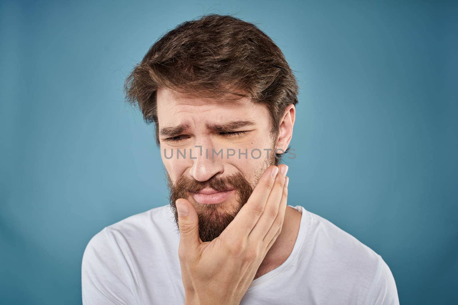 Bearded man displeased facial expression emotions close-up blue background white t-shirt. High quality photo