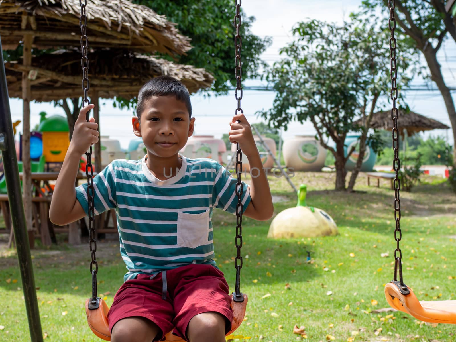 A boy sitting on a swing In the playground by Unimages2527