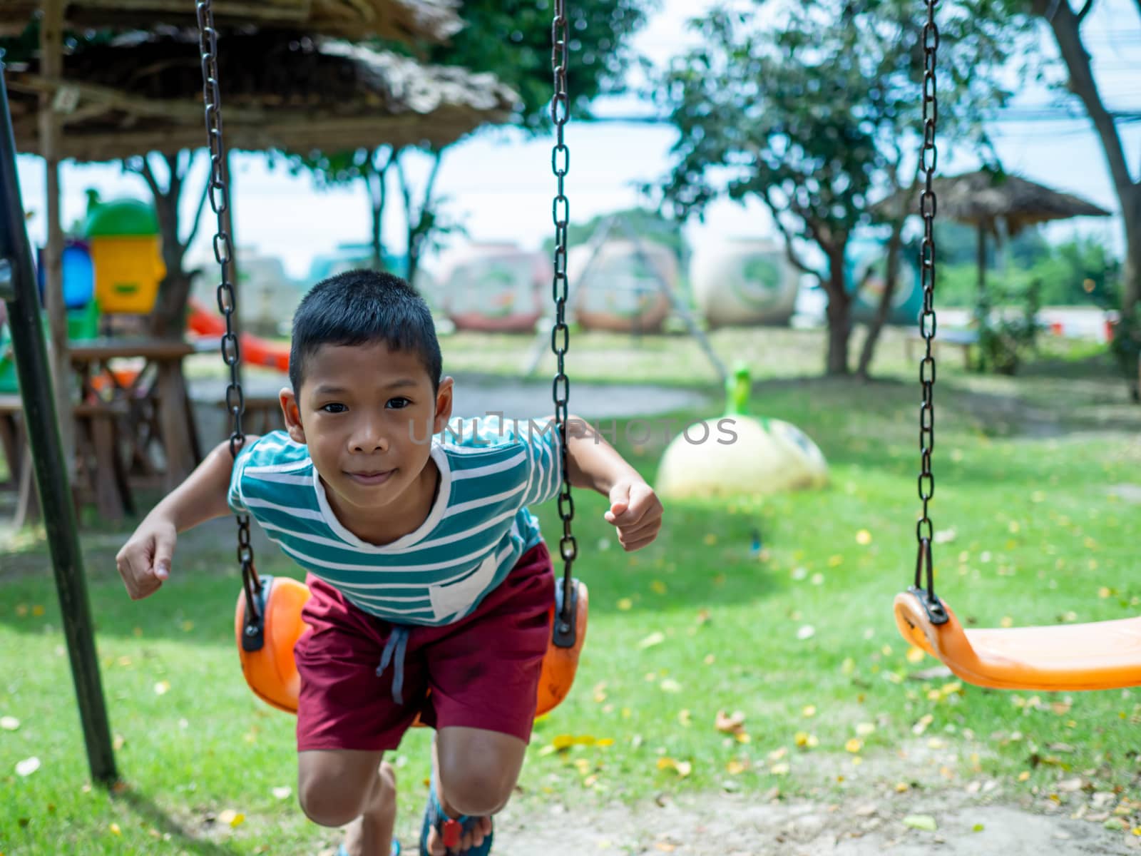 A boy sitting on a swing In the playground by Unimages2527