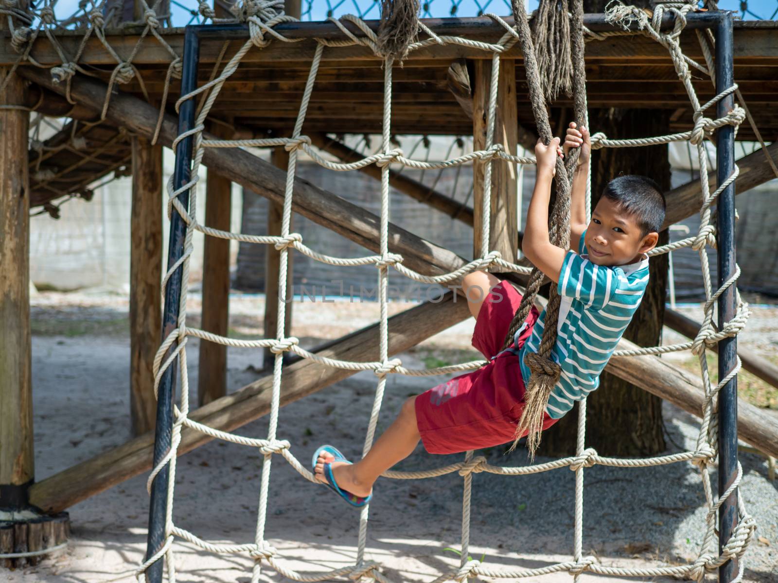 Boy climbing a rope ladder In the playground by Unimages2527