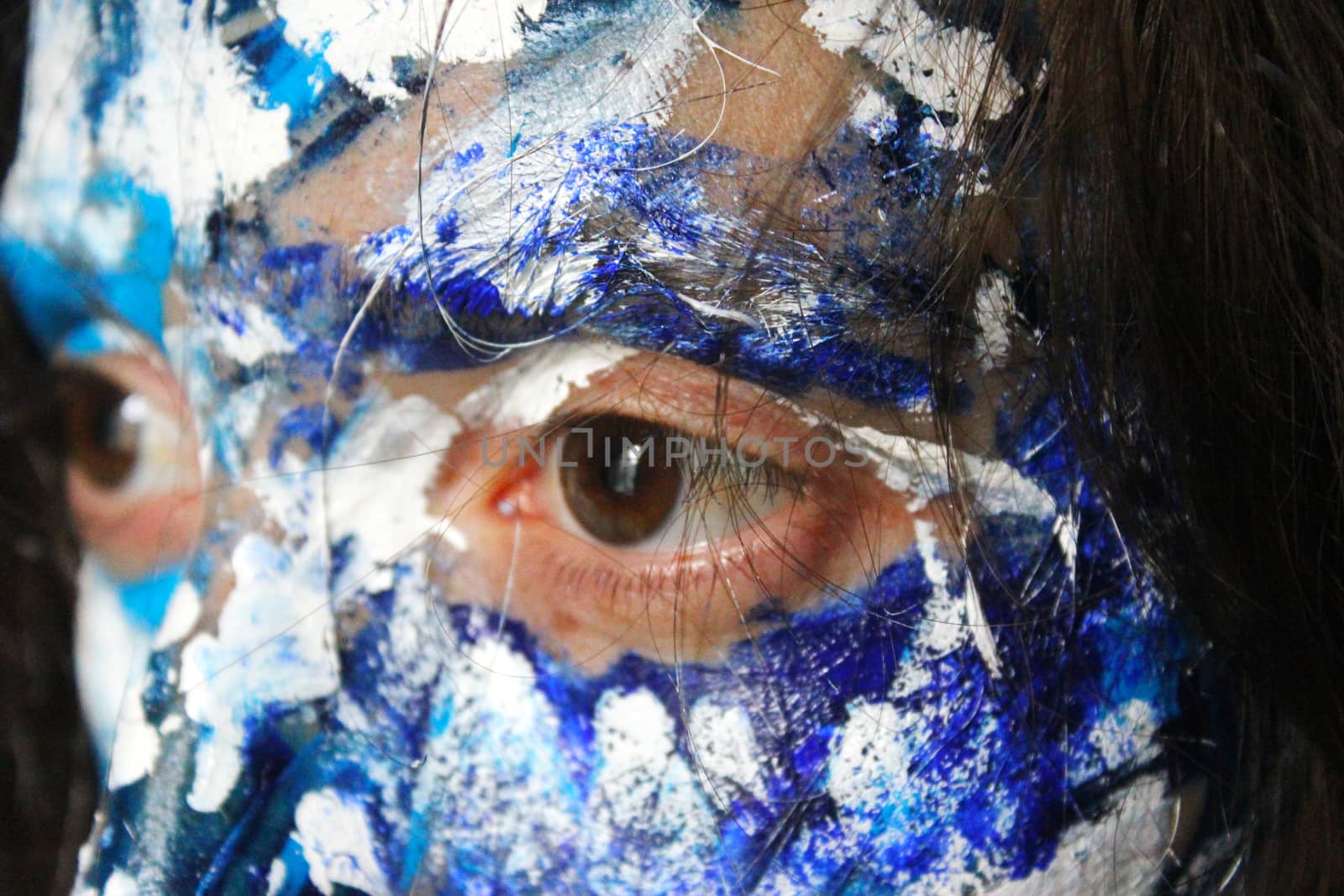 Painted face with acrylic blue and white colors. Young beautiful woman portrait, close-up photo.