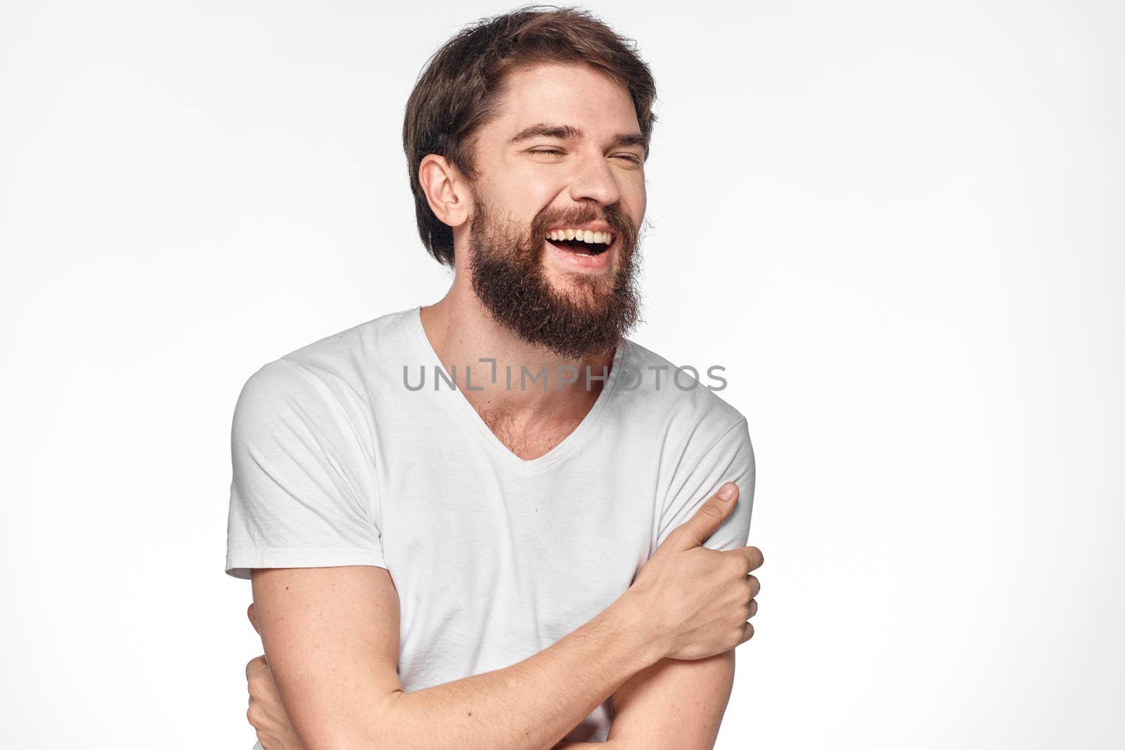 cheerful bearded man in a white t-shirt emotions gestures with his hands light background studio by SHOTPRIME