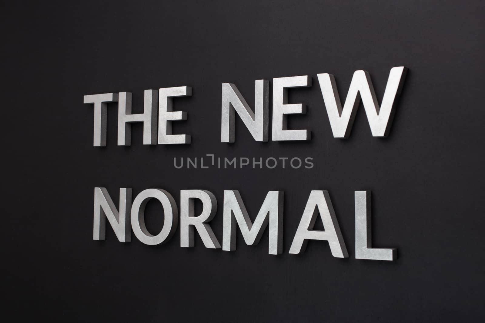 words the new normal laid with silver metal letters on flat black matte surface in tilted perspective with dark lightiing