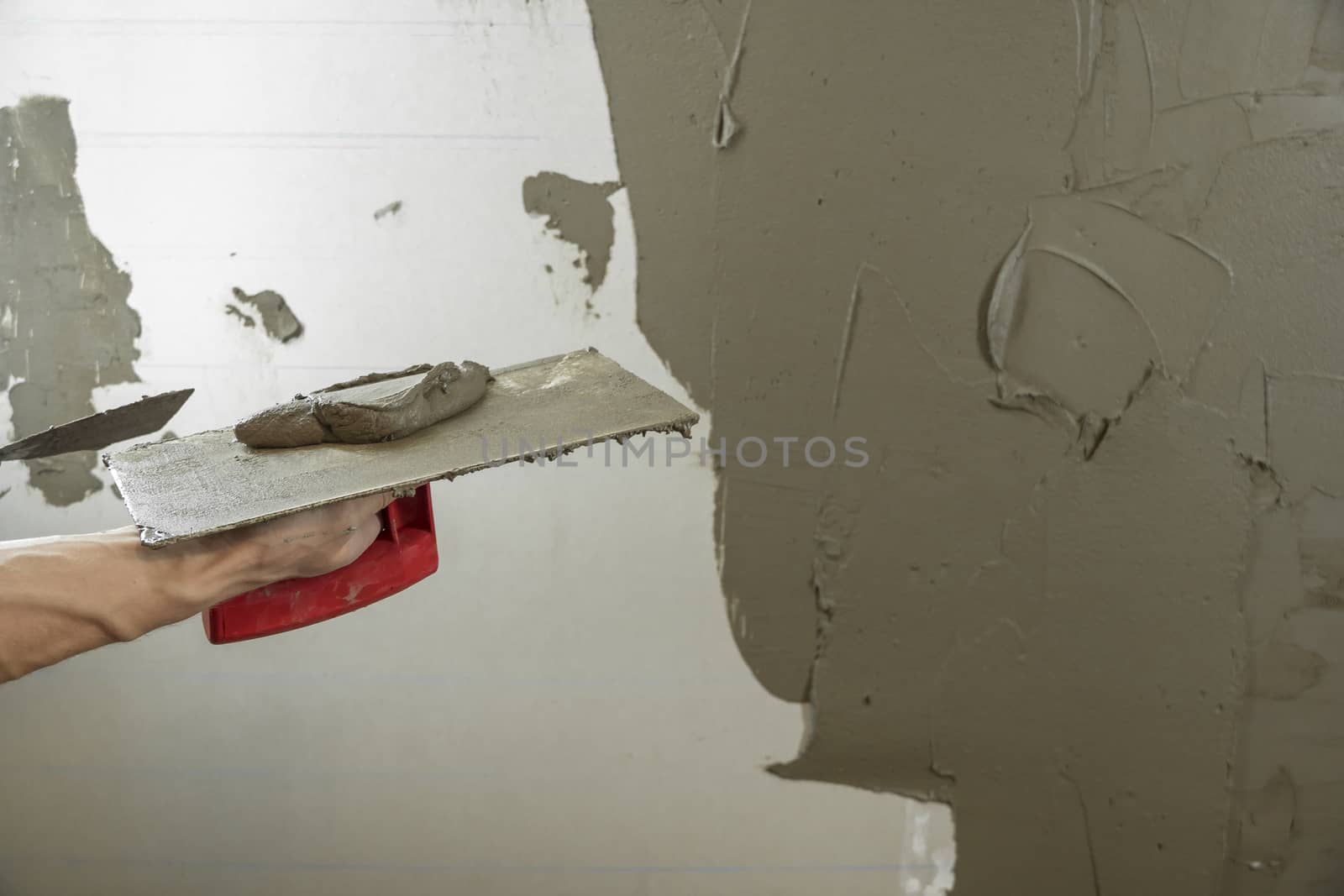 A worker plasters the wall with a spatula and applies a cement mix solution. The repairman lays the plaster on the drywall. Handyman repairs home. Laborer restore dwelling.Specialist covers up cracks