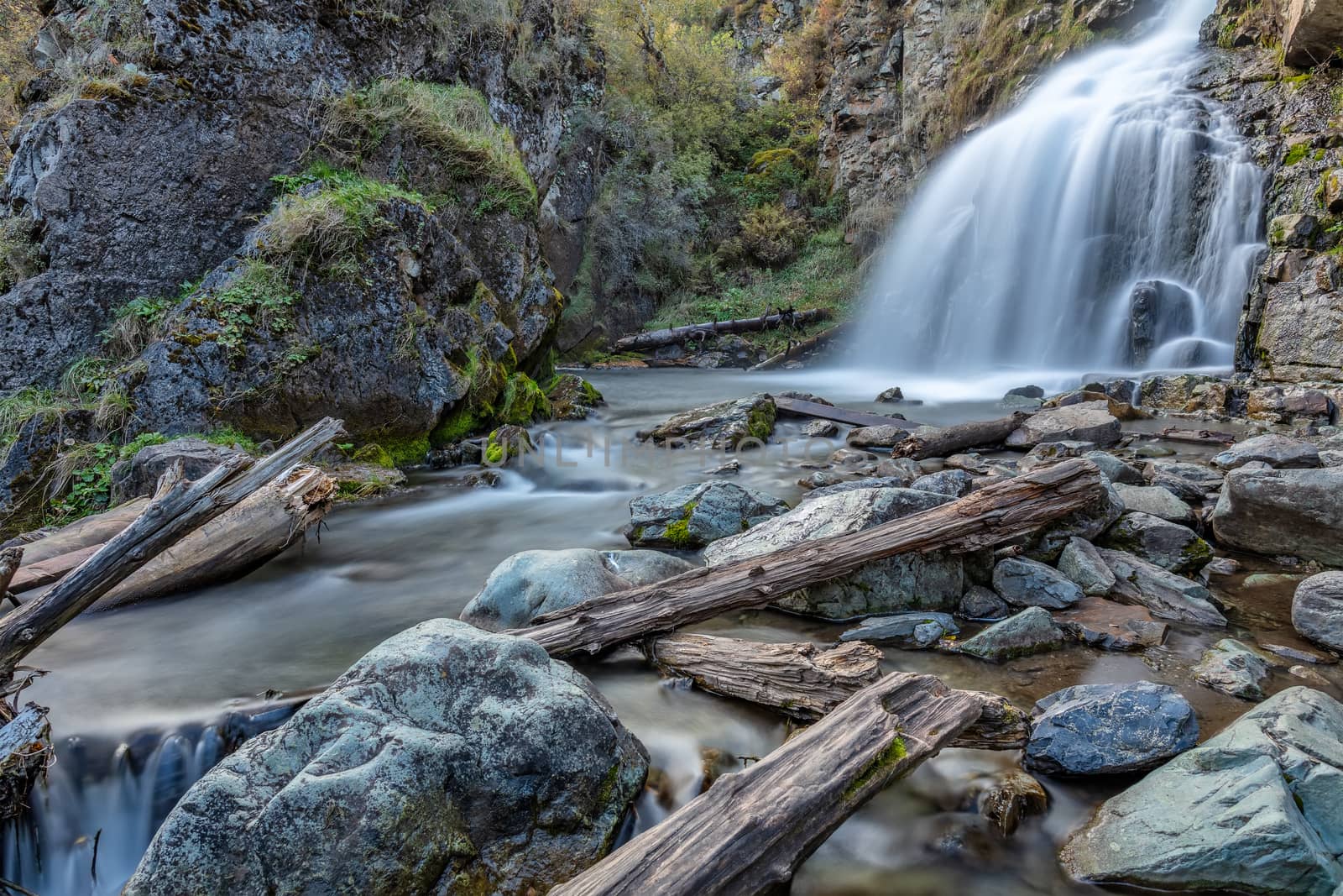 Beautiful shot of Kamischlinskiy waterfall in Altai mountains in Siberia, Russia. Smooth, silky water. Long exposure. Rocks and logs in the foreground.