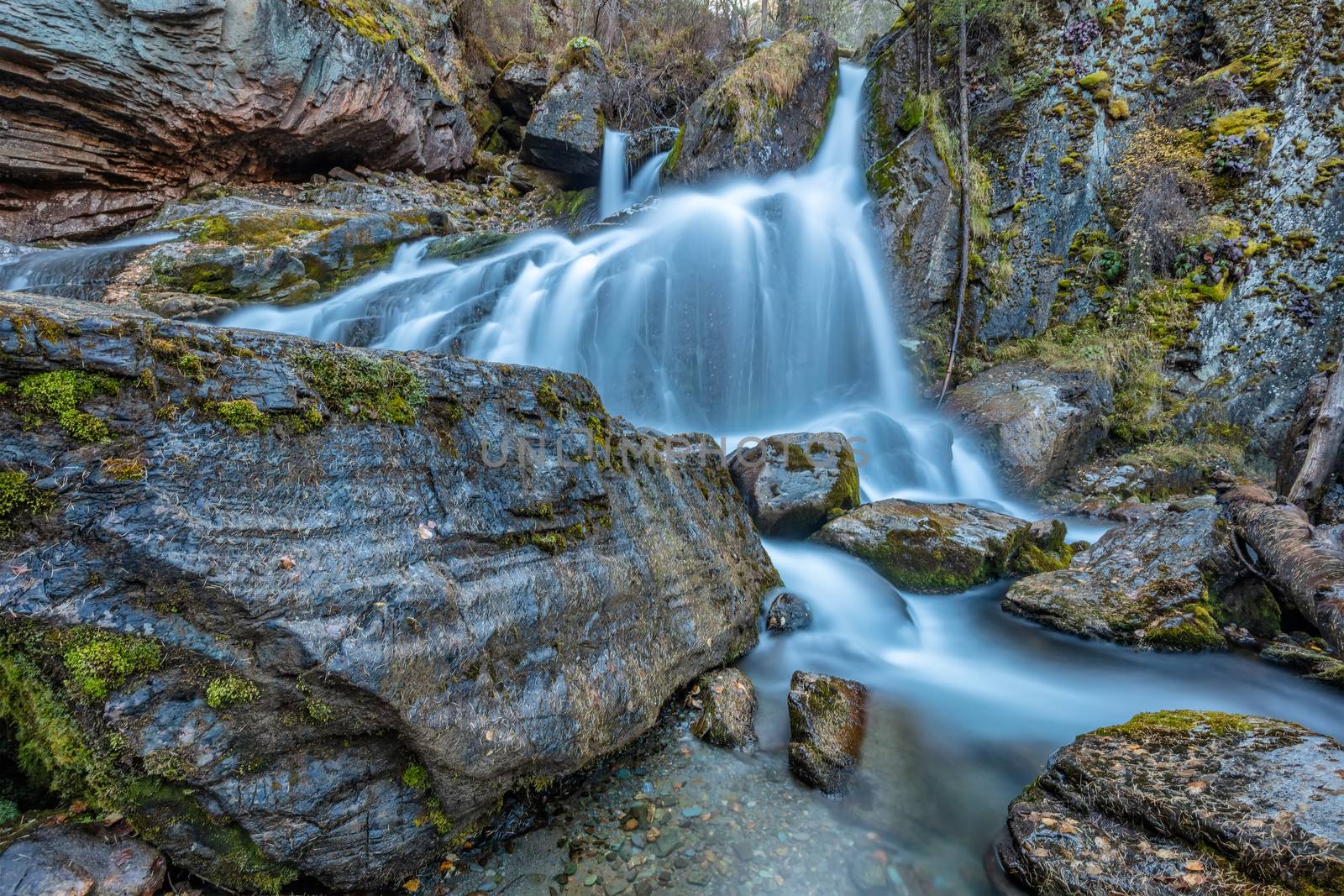 Beautiful shot of waterfall in Altai mountains in Siberia, Russia. Smooth, silky water. Long exposure. Rocks and logs in the foreground.