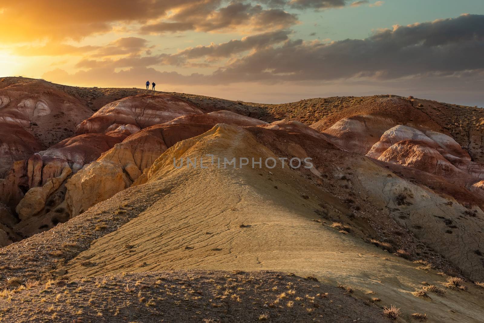 Beautiful low angle shot of two tiny human figures walking towards sunset on top of massive red mountain in Kyzyl-Chin valley, also called Mars valley. Golden hour. Altai, Siberia, Russia by DamantisZ