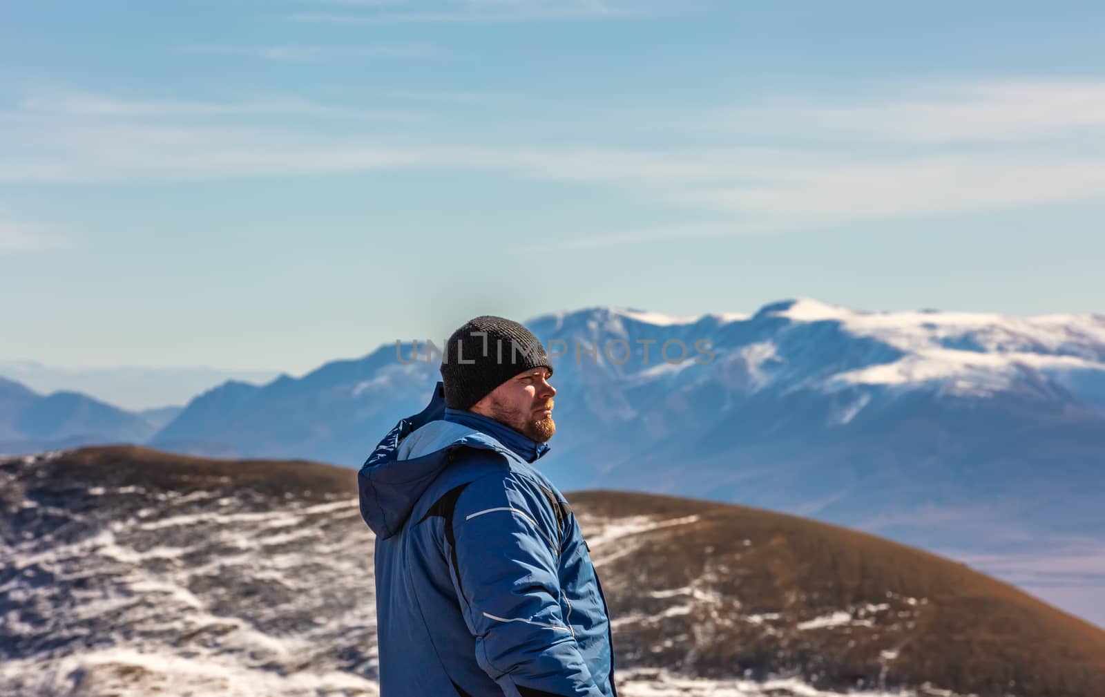 View of a tourist looking in the distance in the mountains. White snowy mountain ridge and beautiful blue cloudy sky as a background and slightly out of focus. Altai mountains, Siberia, Russia.