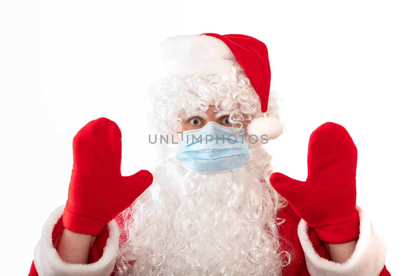 View of a man wearing a Santa Claus costume, medical mask and having his both hands up, eyes wide open, as if warning or stopping something, isolated on white background. Pandemic holiday concepts.
