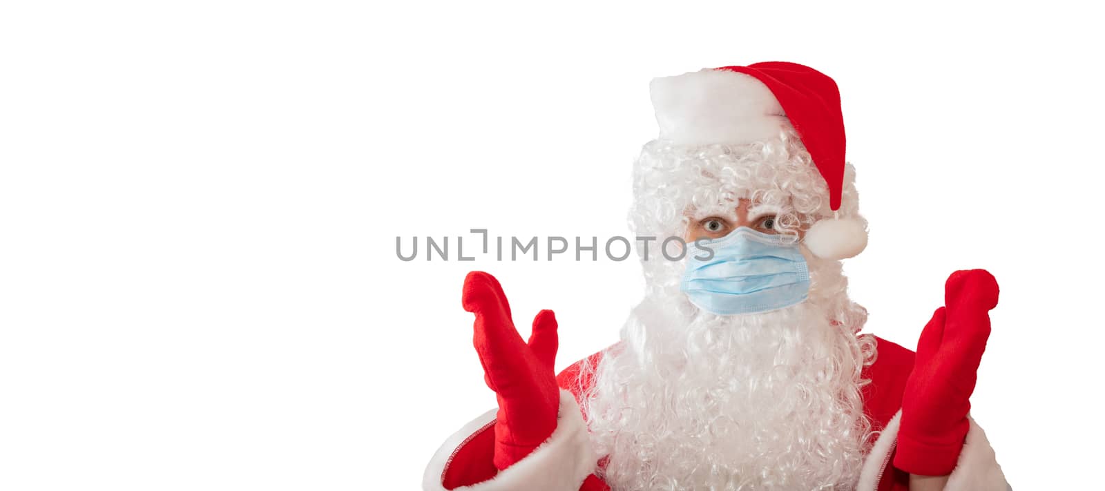 View of a man wearing a Santa Claus costume and medical mask with his arms, eyes wide open, isolated on white background. Man is upset. Banner size, copy space. New normal, pandemic holiday concepts.