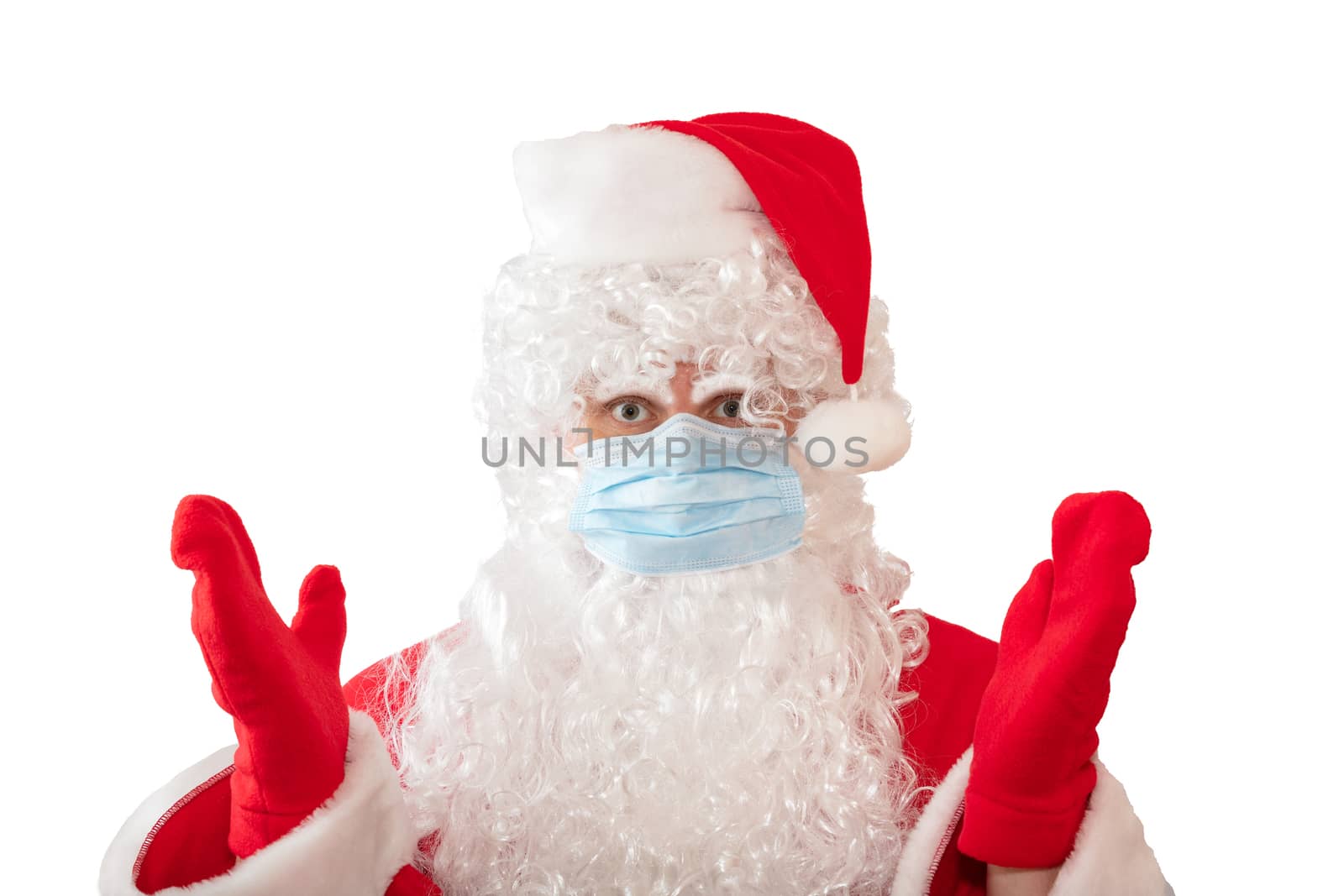 View of a man wearing a Santa Claus costume and medical mask with his arms and eyes wide open, isolated on white background. Man looks upset. New normal, new reality, pandemic holiday concepts by DamantisZ