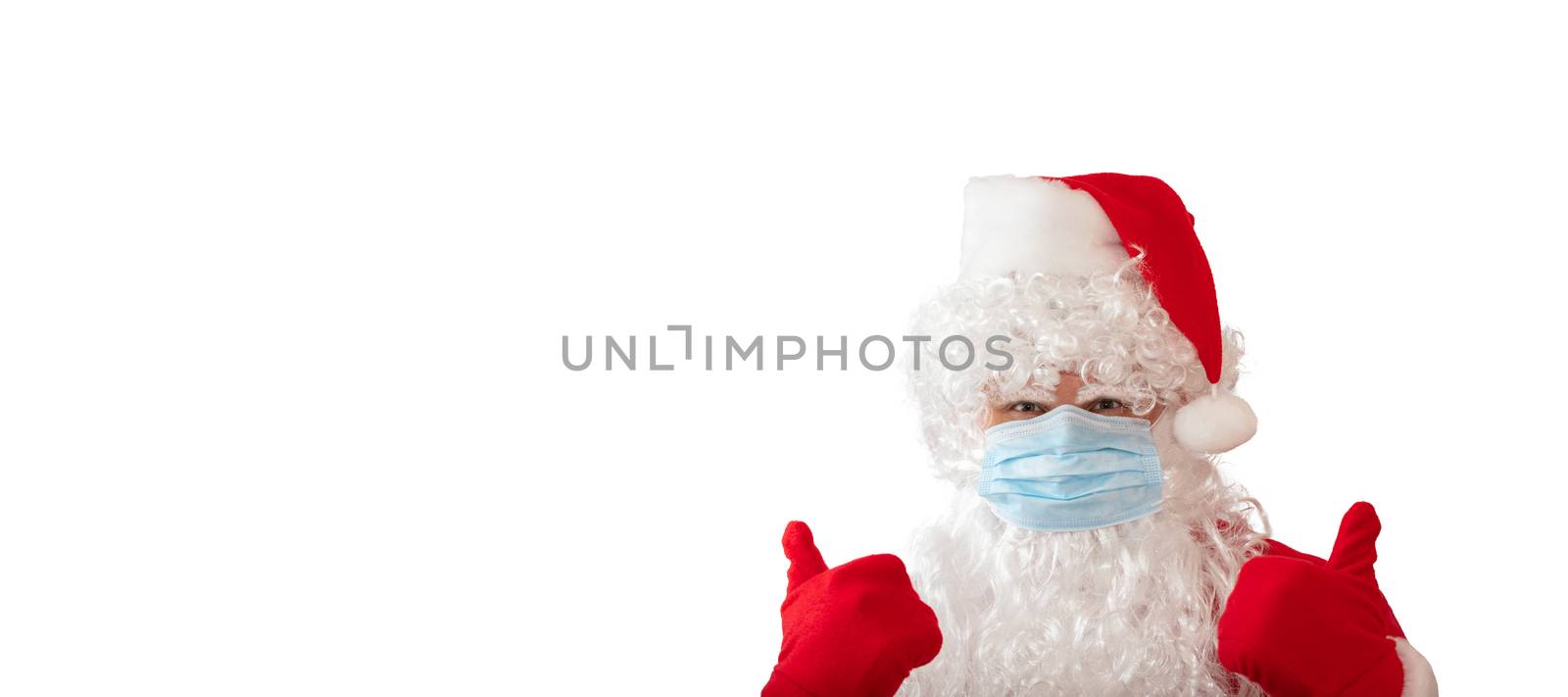View of a man wearing a Santa Claus costume and medical mask with his thumbs up, isolated on white background. Man looks stressed. Banner size, copy space. New normal, pandemic holiday concepts by DamantisZ