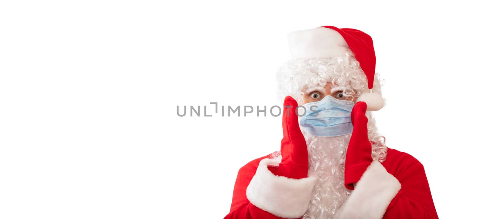 View of a man wearing a Santa Claus costume, medical mask with his arms by his face, eyes wide open, isolated on white background. Man looks scared. Banner size, copy space. Pandemic holiday concept.