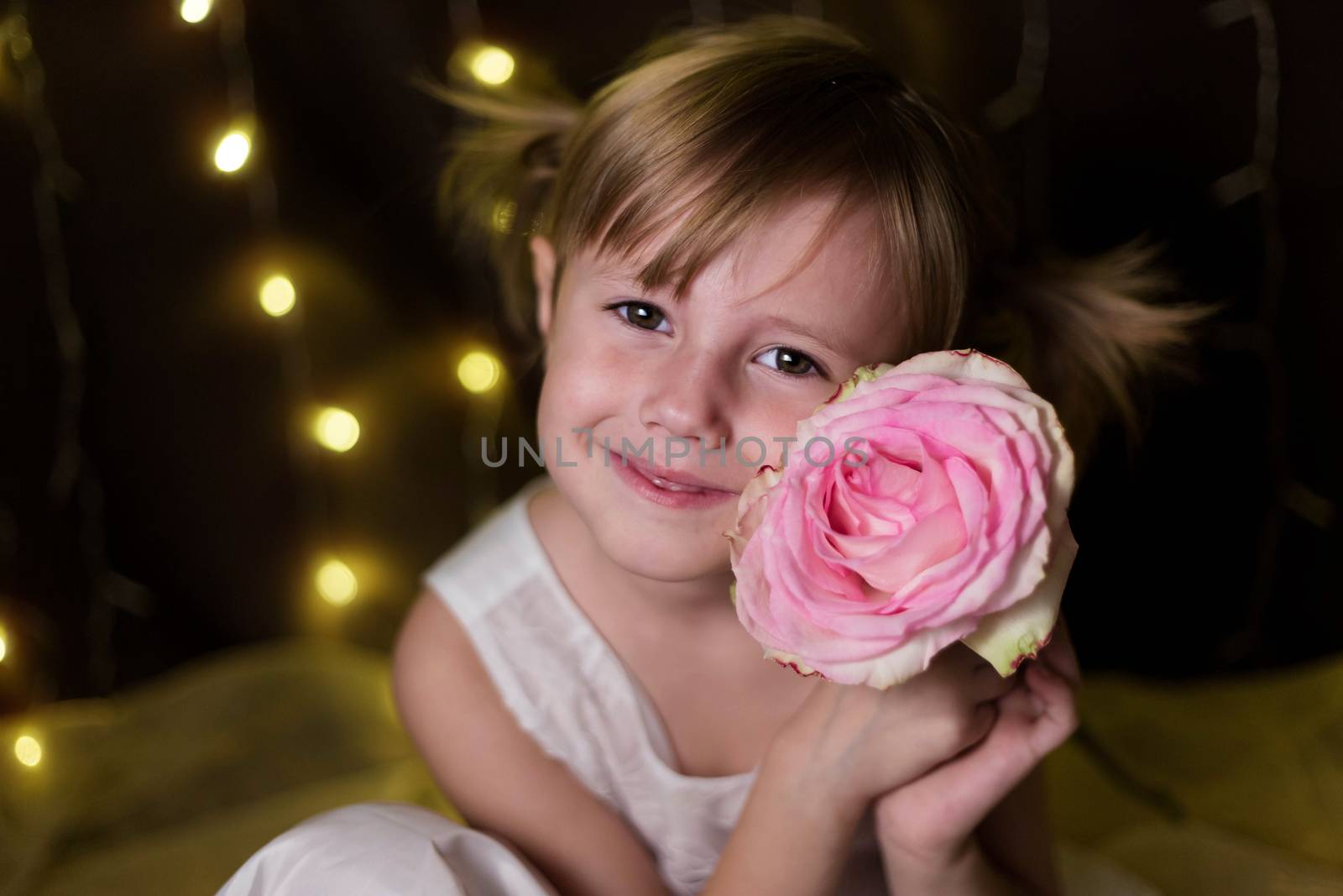 Young adorable pretty girl with rose from her father over dark background with garlands bokeh