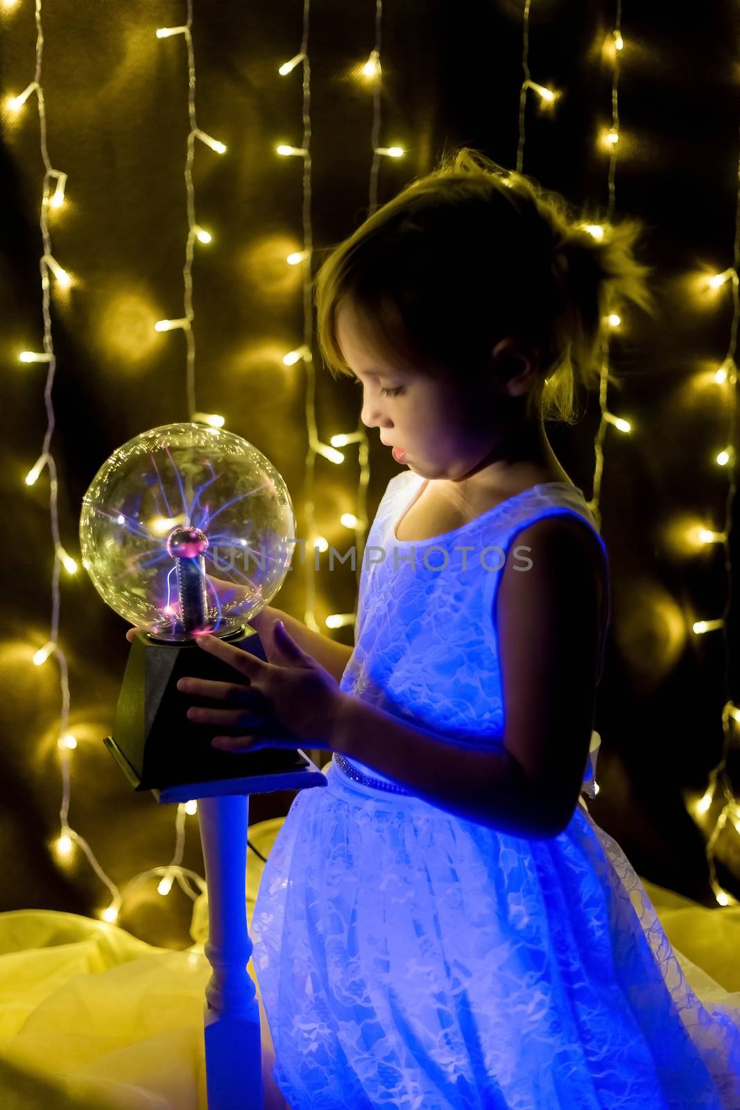 Cute little Child girl holding witch crystal ball with lightning and electricity over dark background with garlands bokeh