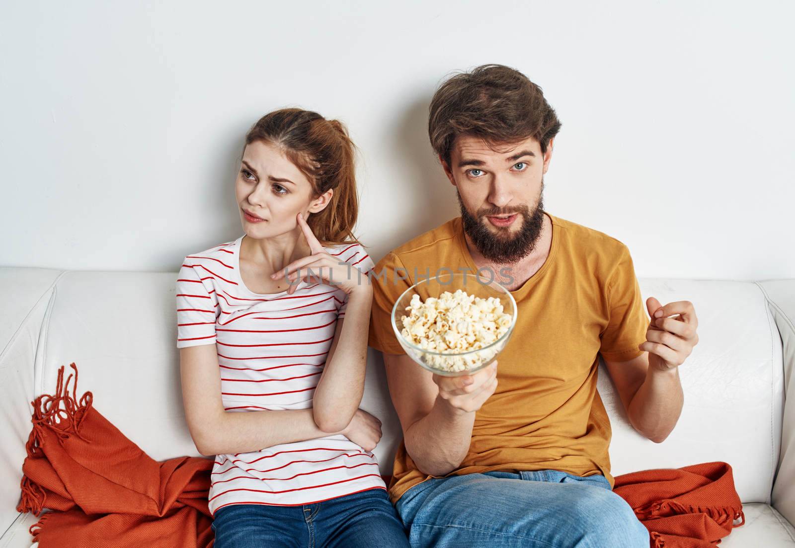A man and a woman on the couch watching TV with popcorn in a plate. High quality photo