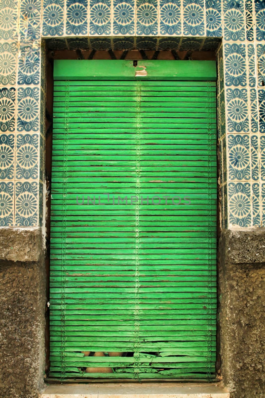 Old and damaged tiled facade in Lisbon. Closed Window with green blind