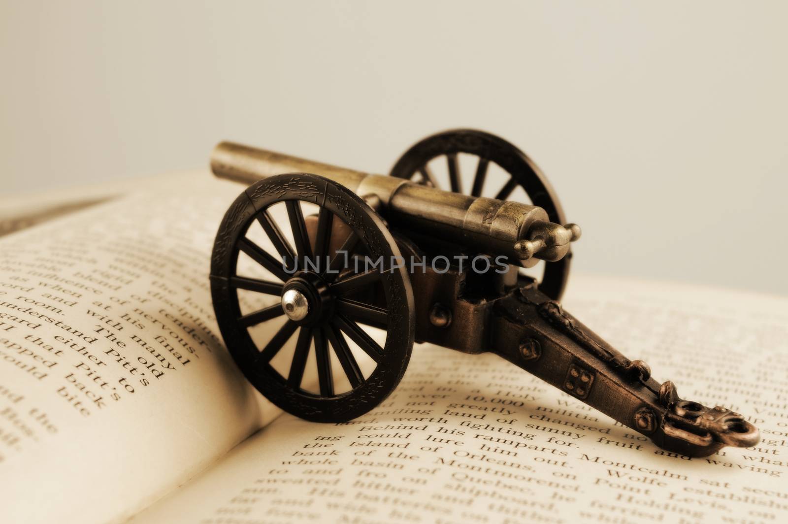 Closeup of an open book with a war cannon ontop using a vintage effect.