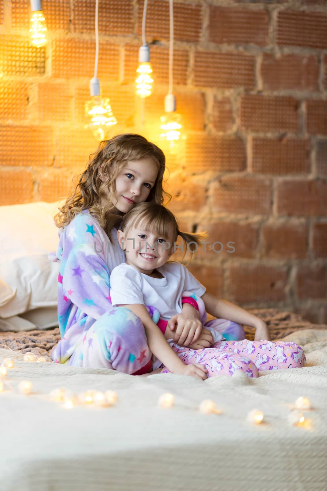 Little sisters in pajamas on the bed smiling and christmas garlands by galinasharapova