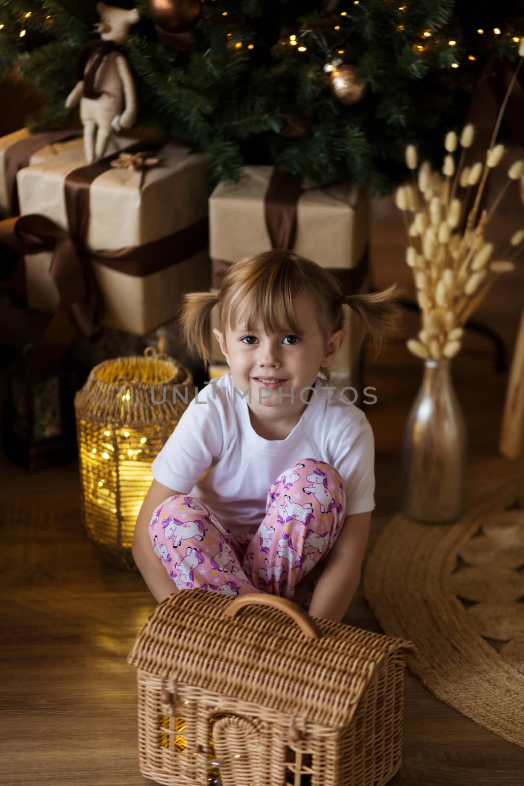 .Girl in pajamas sits on the floor in front of the Christmas tree and plays.