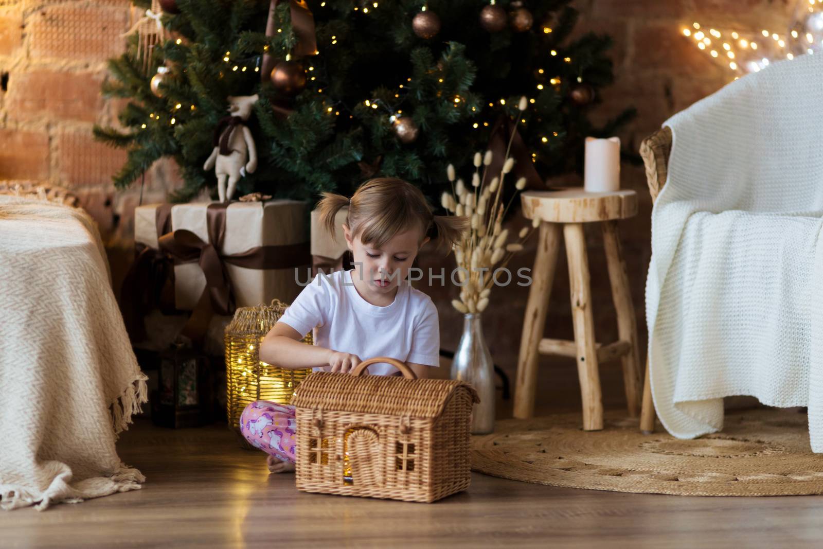 .Girl in pajamas sits on the floor in front of the Christmas tree and plays.