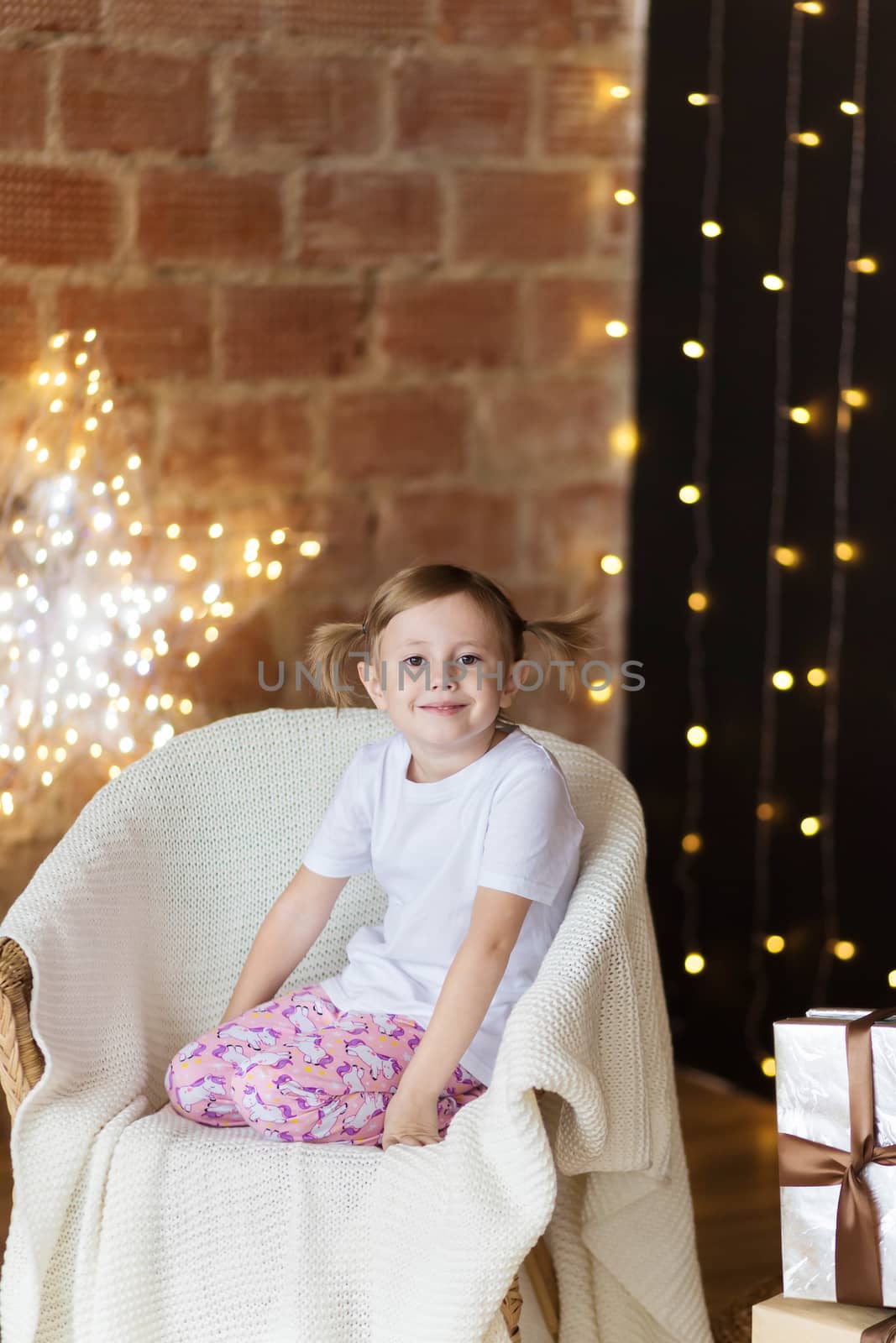 Beautiful child with a christmas gift in pajamas sitting on the chair looking at the camera